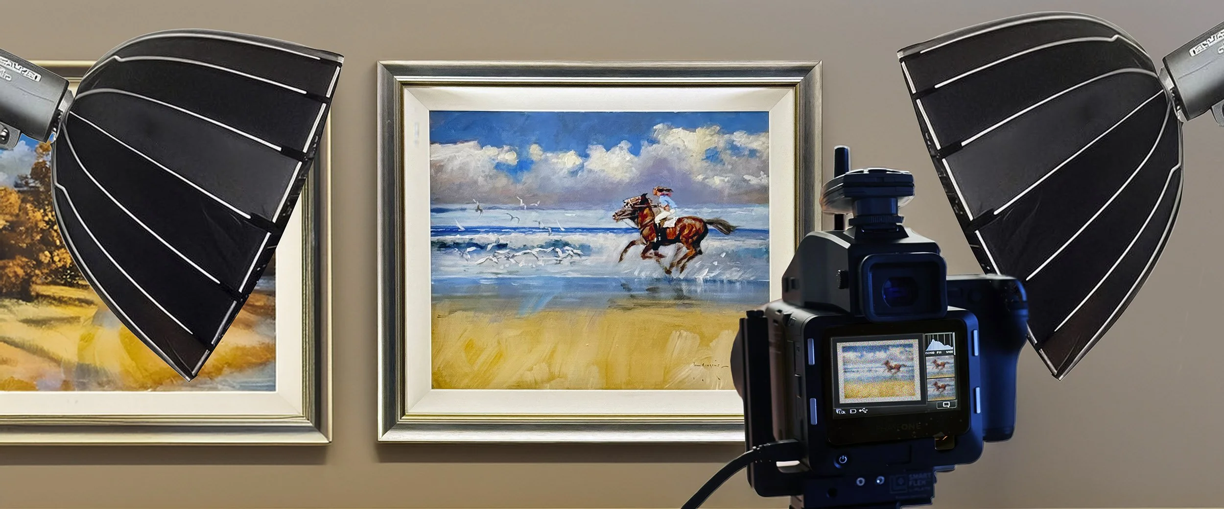 A camera positioned in front of a painting of a person riding a horse along the beach, with seagulls flying in the sky.