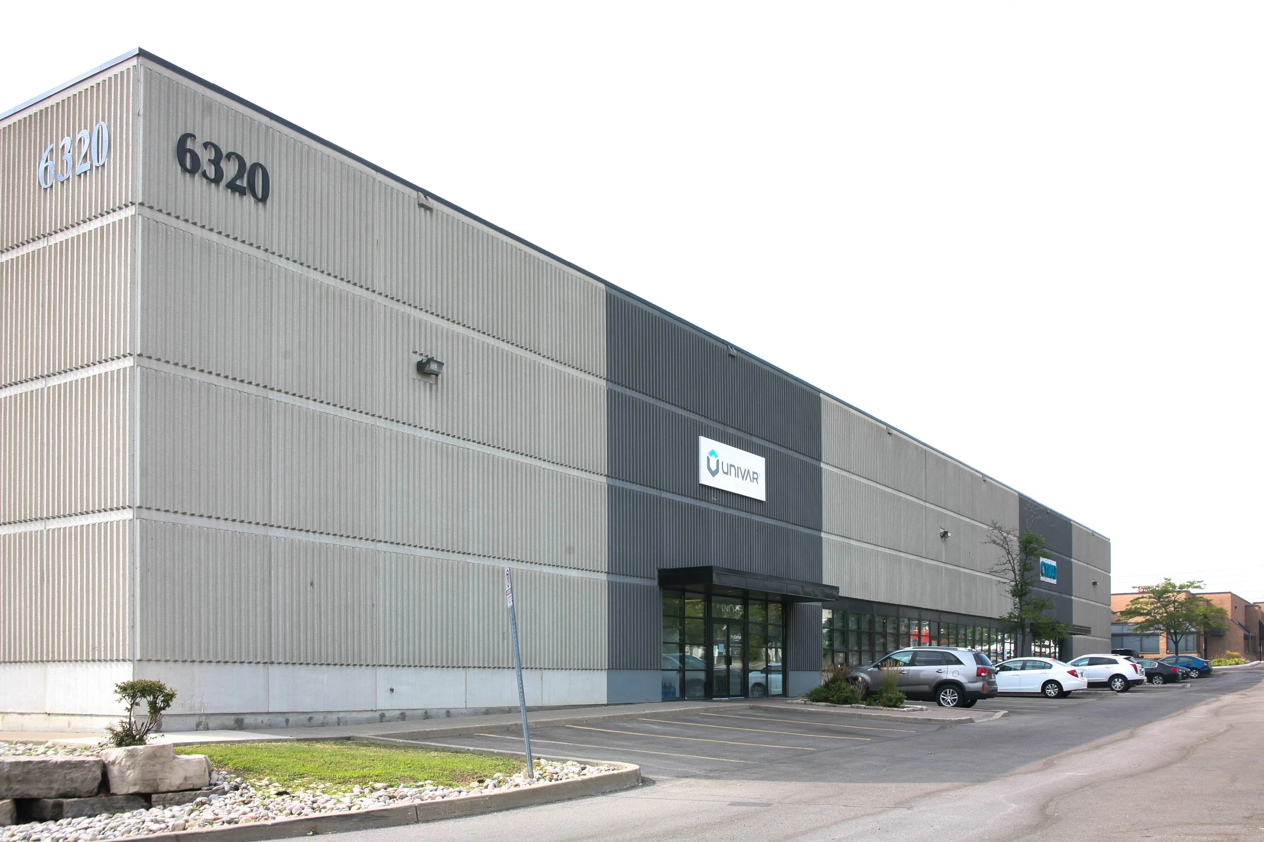 Exterior view of a commercial building with the company logos "6320" and "UNIVAR" on the facade, parking lot with several cars in front, and a clear sky.