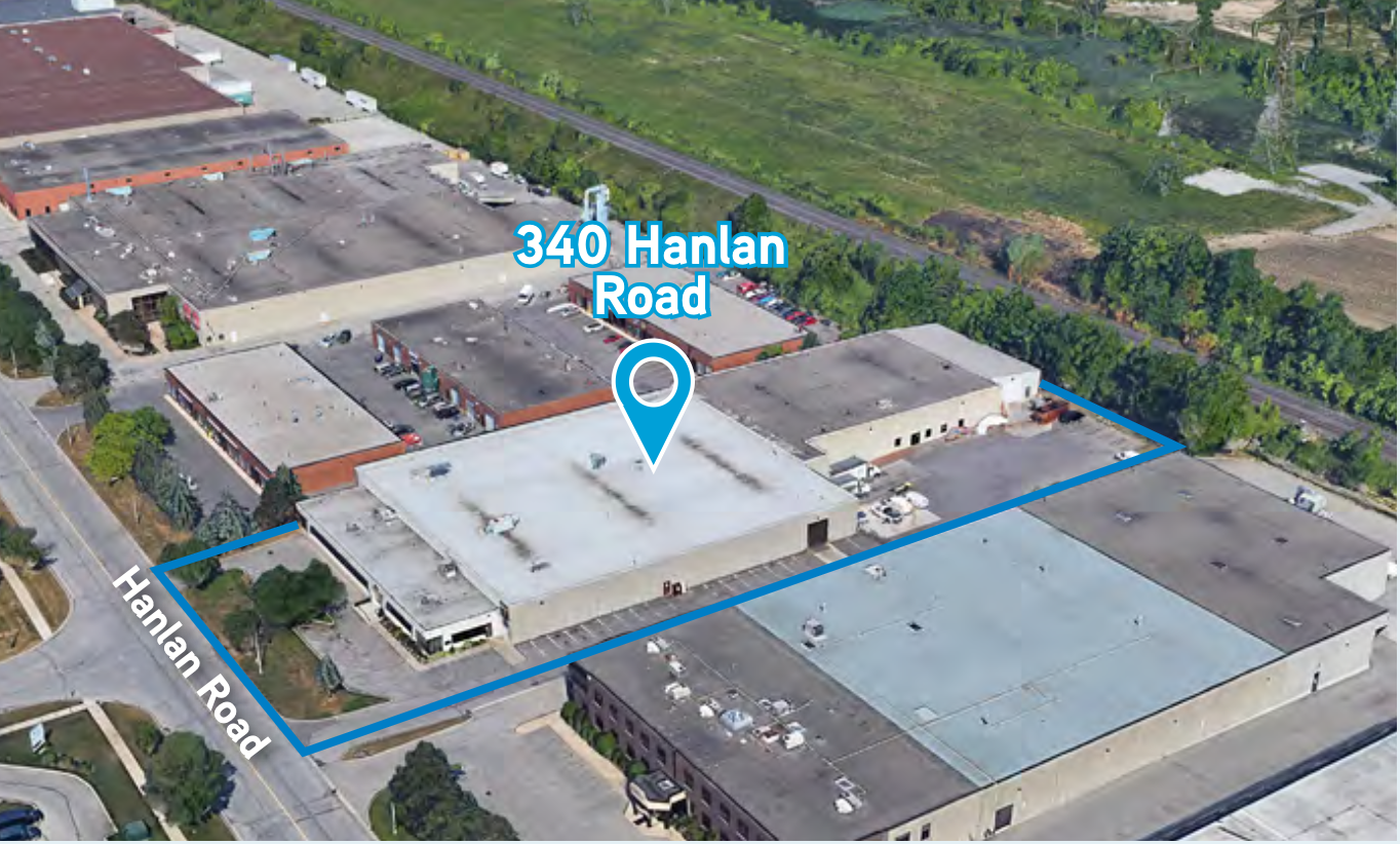 Aerial view of a commercial building complex with a sign indicating 340 Hanlan Road, with surrounding parking lots and nearby green areas.