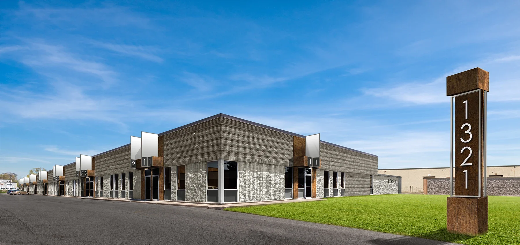Exterior view of a modern commercial building with a sign displaying street number 1321, a grassy lawn, and parking lot, under a blue sky with some clouds.