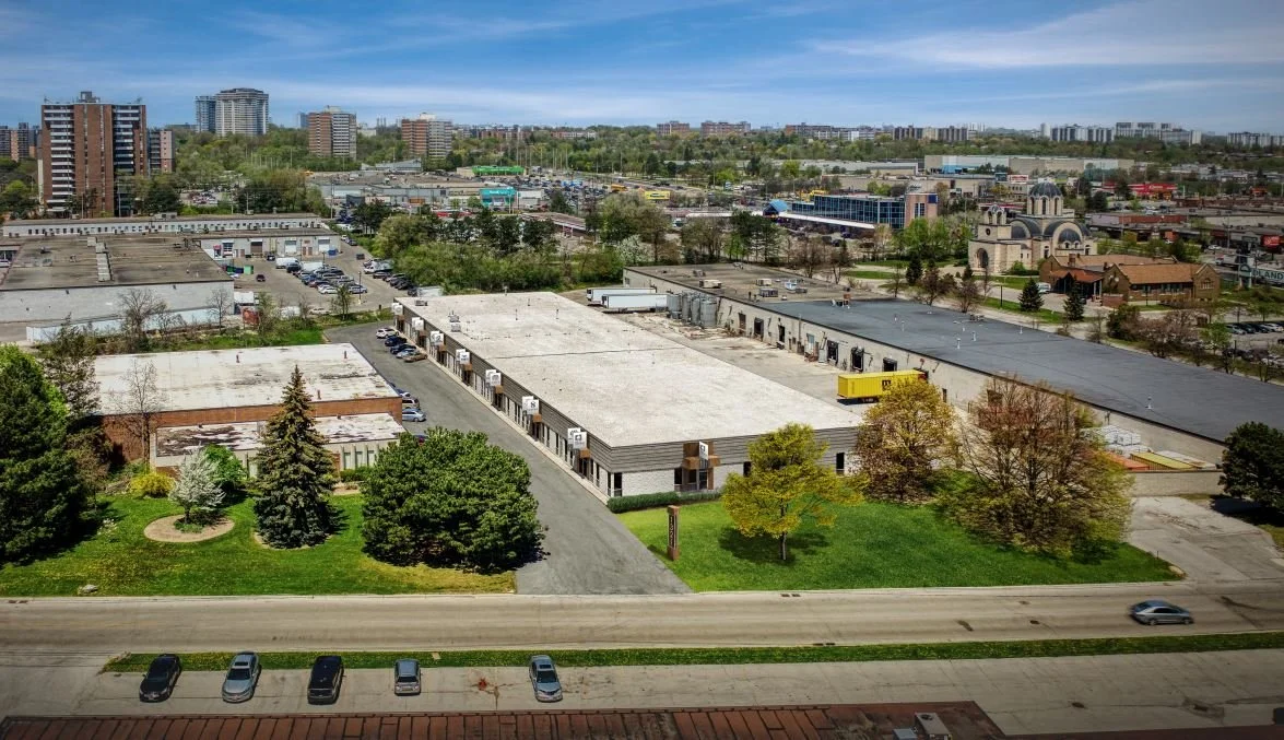 Aerial view of commercial buildings, parking lots, and green spaces in an urban area on a partly cloudy day.