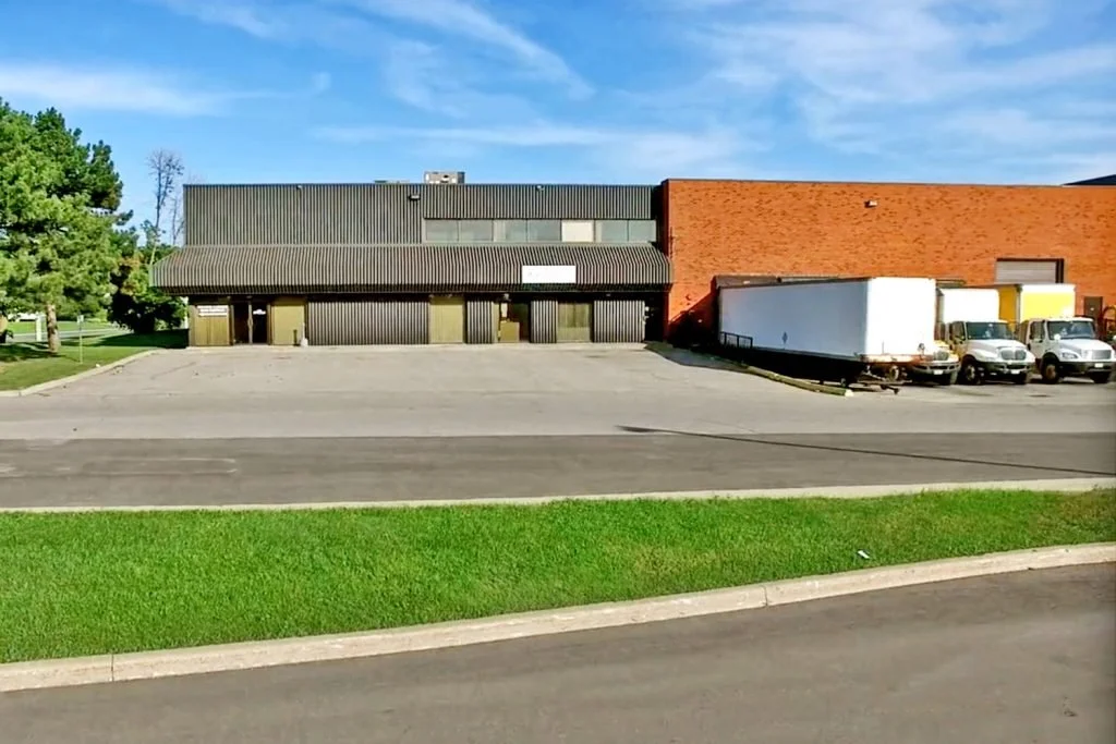 View of a parking lot in front of a commercial building with a mix of black and red brick exterior walls and several parked trucks and vehicles.