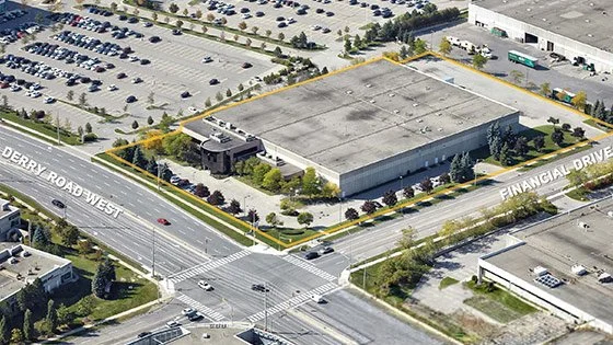 An aerial view of a large commercial building surrounded by parking lots and roads, with a fenced area around the building outlining its perimeter.