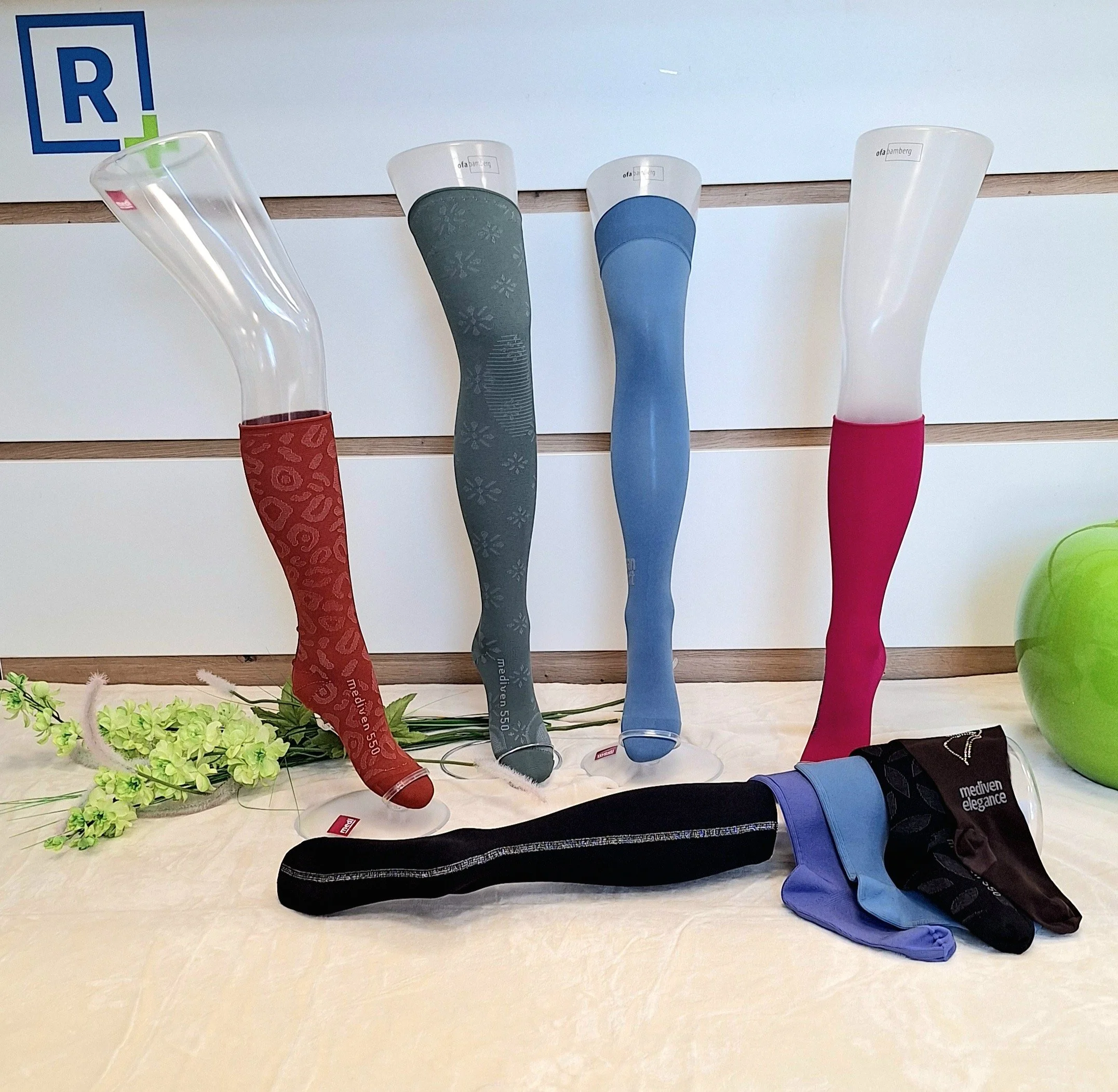 Drei längliche, bunte, deformierte Glasvasen mit unterschiedliche Muster, die auf einer Holz- und Stoffoberfläche stehen. Sie sind mit bunte Socken bedeckt, die die oberen Enden der Vasen bedecken.