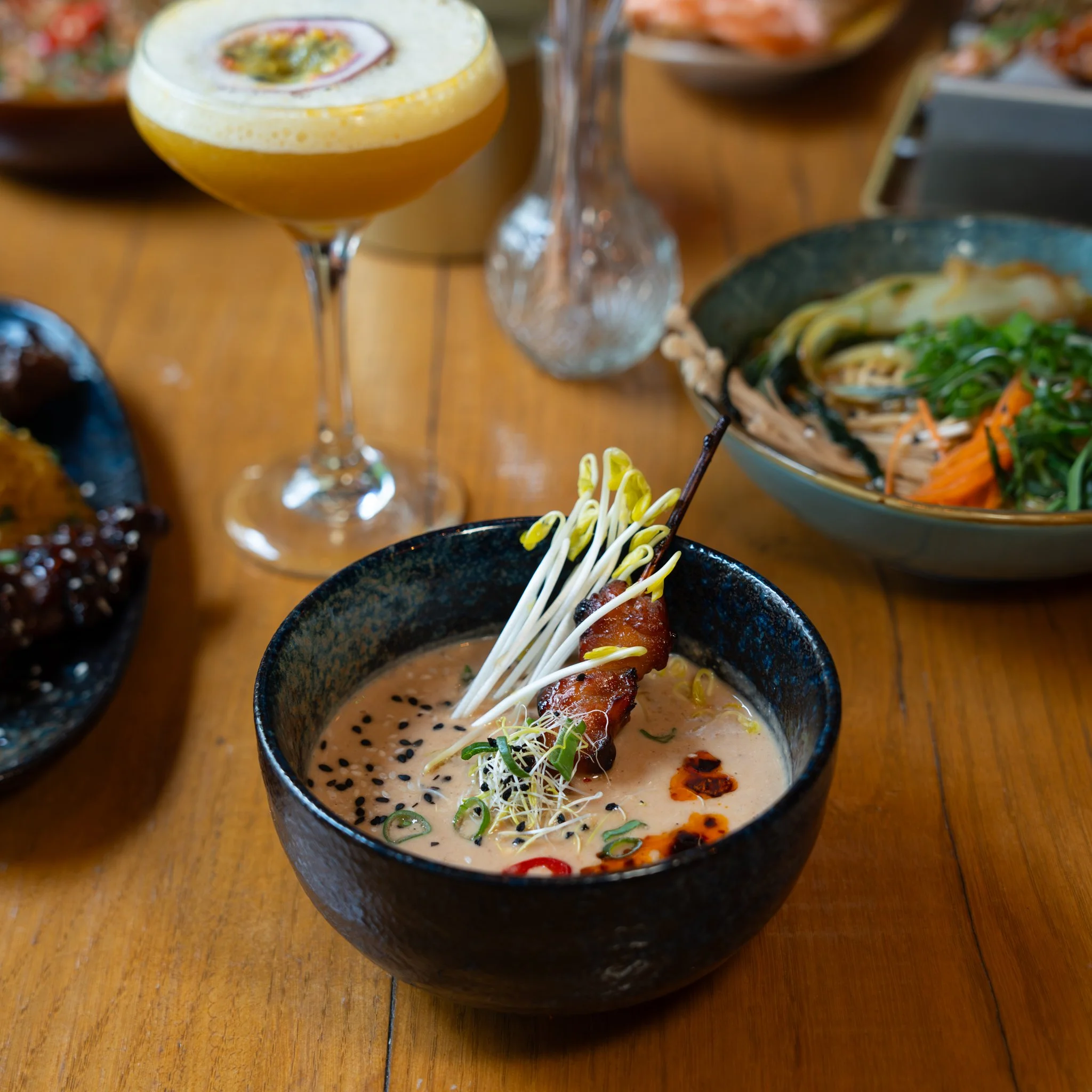 A bowl of creamy soup with garnishes and a cocktail glass on a wooden table.