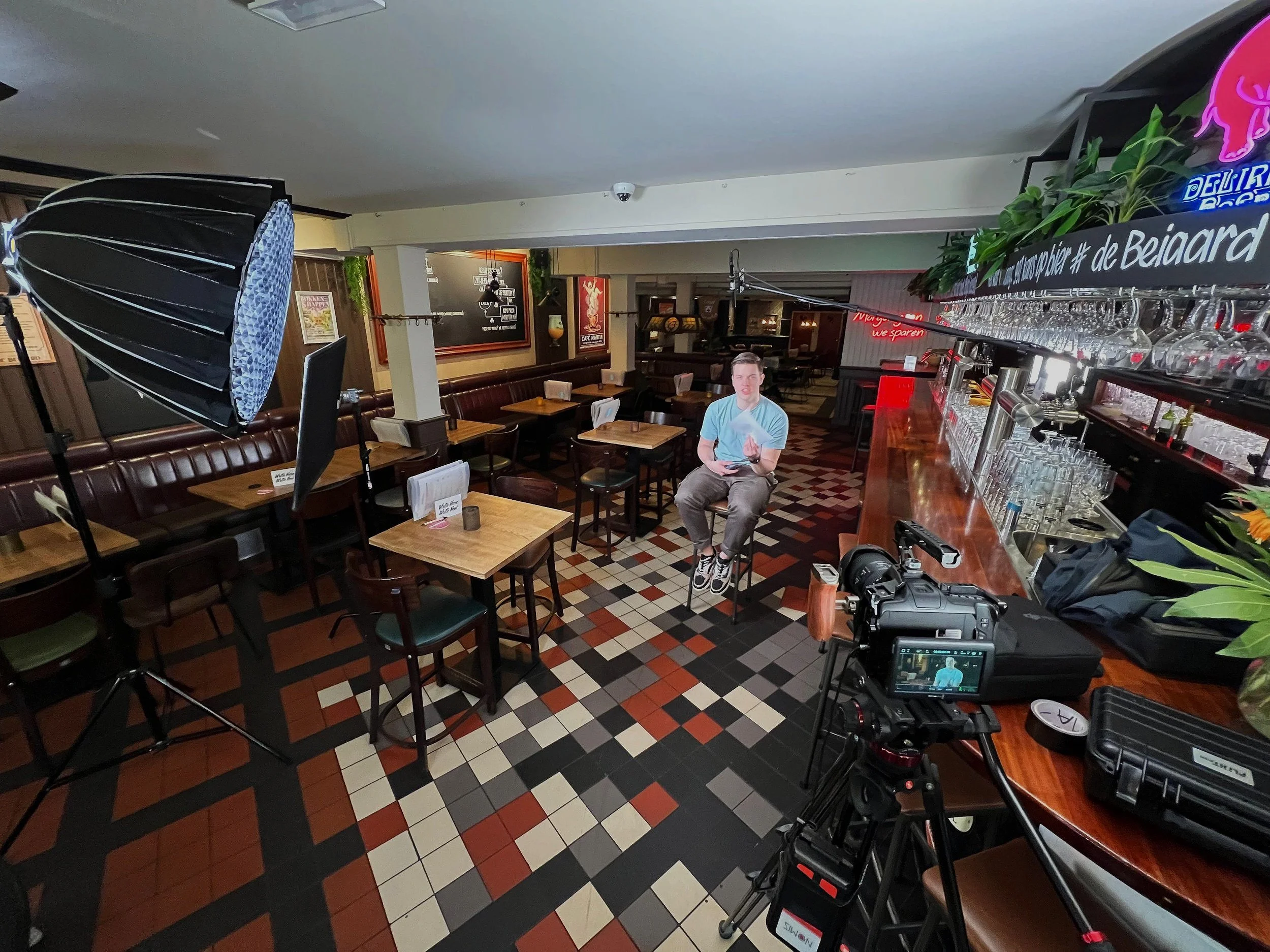 Interior of a bar with a video interview setup, including camera, lights, and a person sitting on a stool.