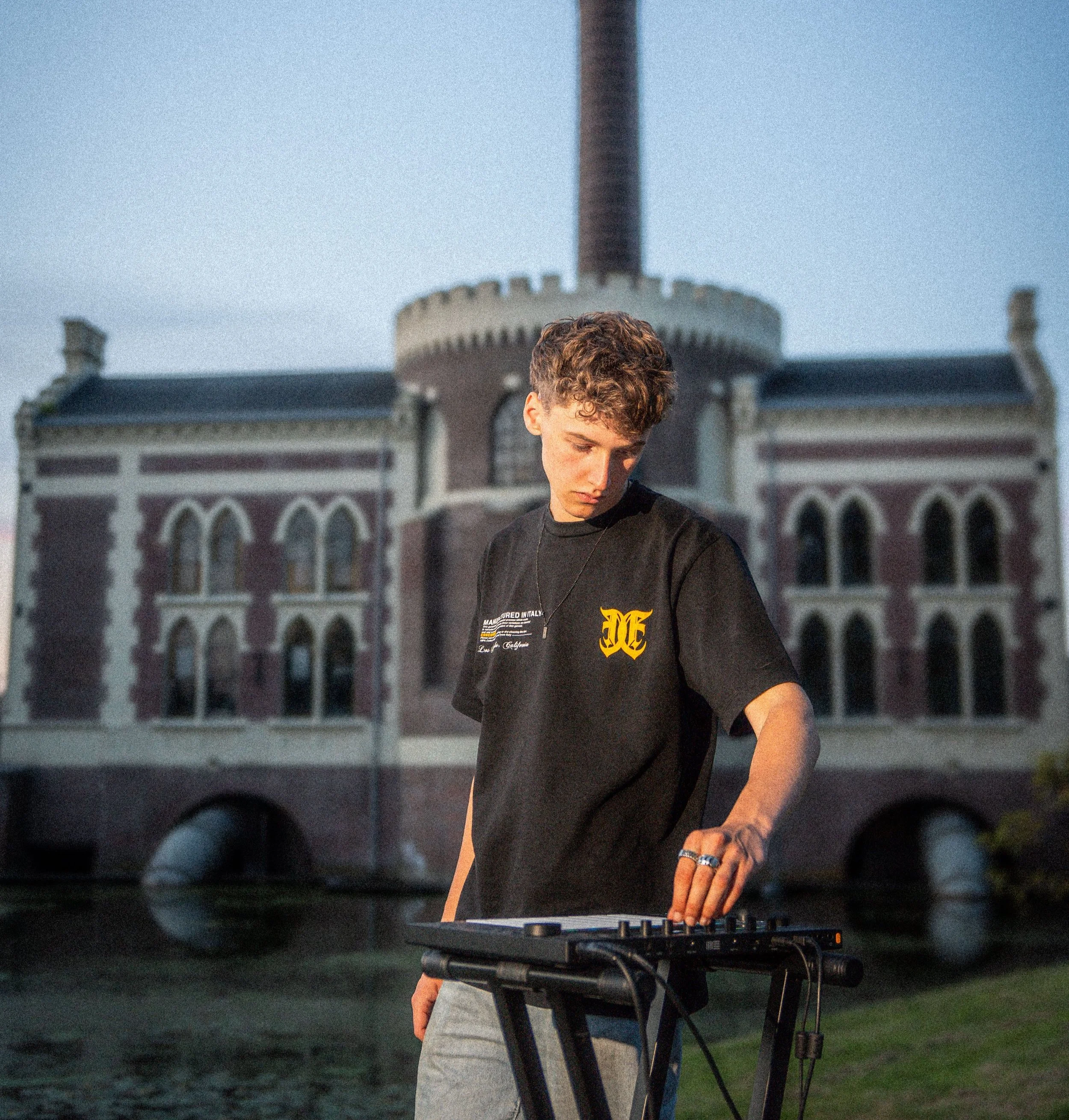 Person using a MIDI controller in front of a historic building with arched windows and a tall chimney.