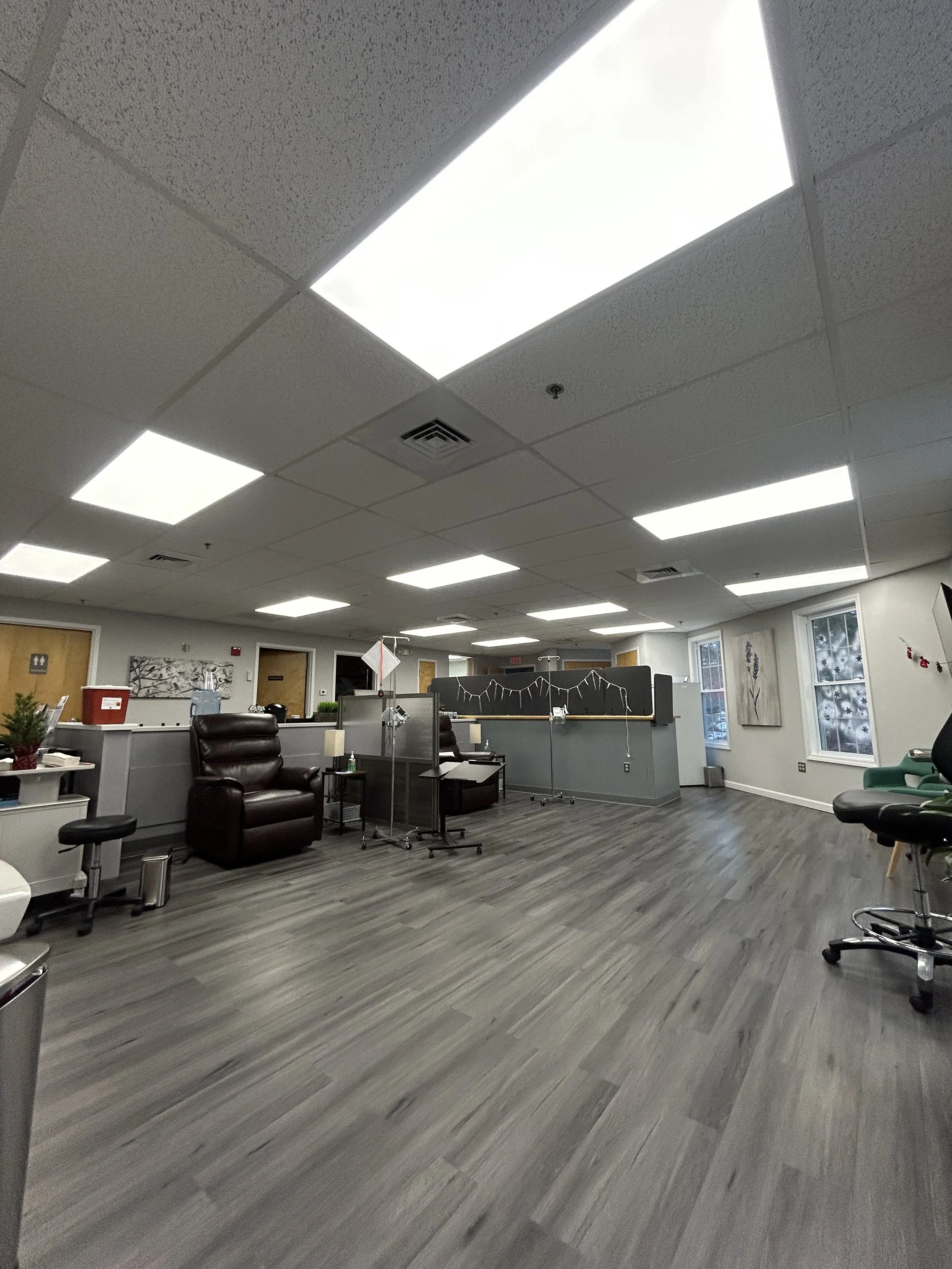 An empty office with gray walls and ceiling, fluorescent lights, a gray wood laminate floor, desks, chairs, and windows with snow outside.