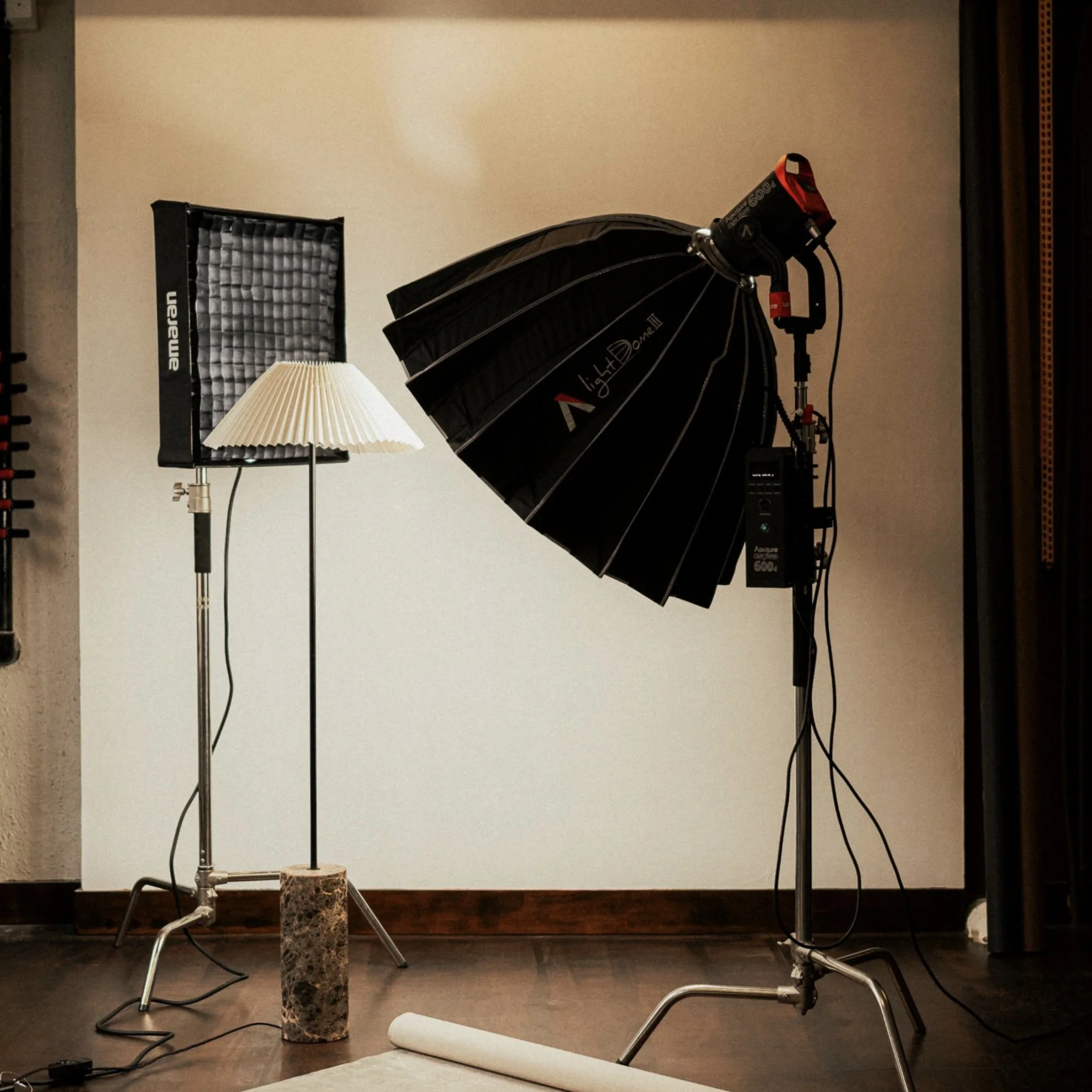 Photography studio setup with professional lighting equipment, including a large black softbox, a smaller white lamp, and a reflector, set against a plain background.