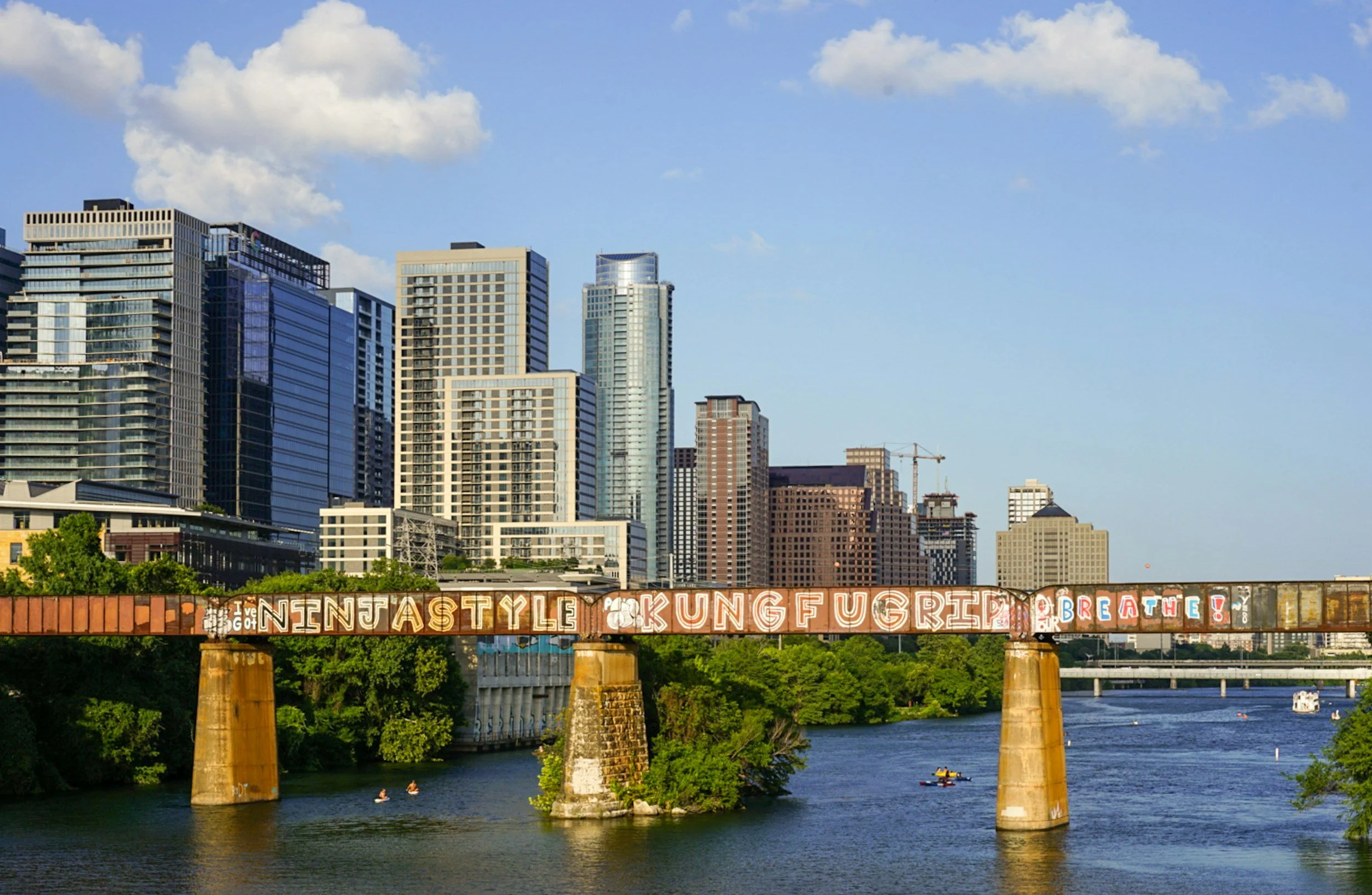 Austin skyline and the train tressel over Lady Bird Lakeduring the daytime with blue skies