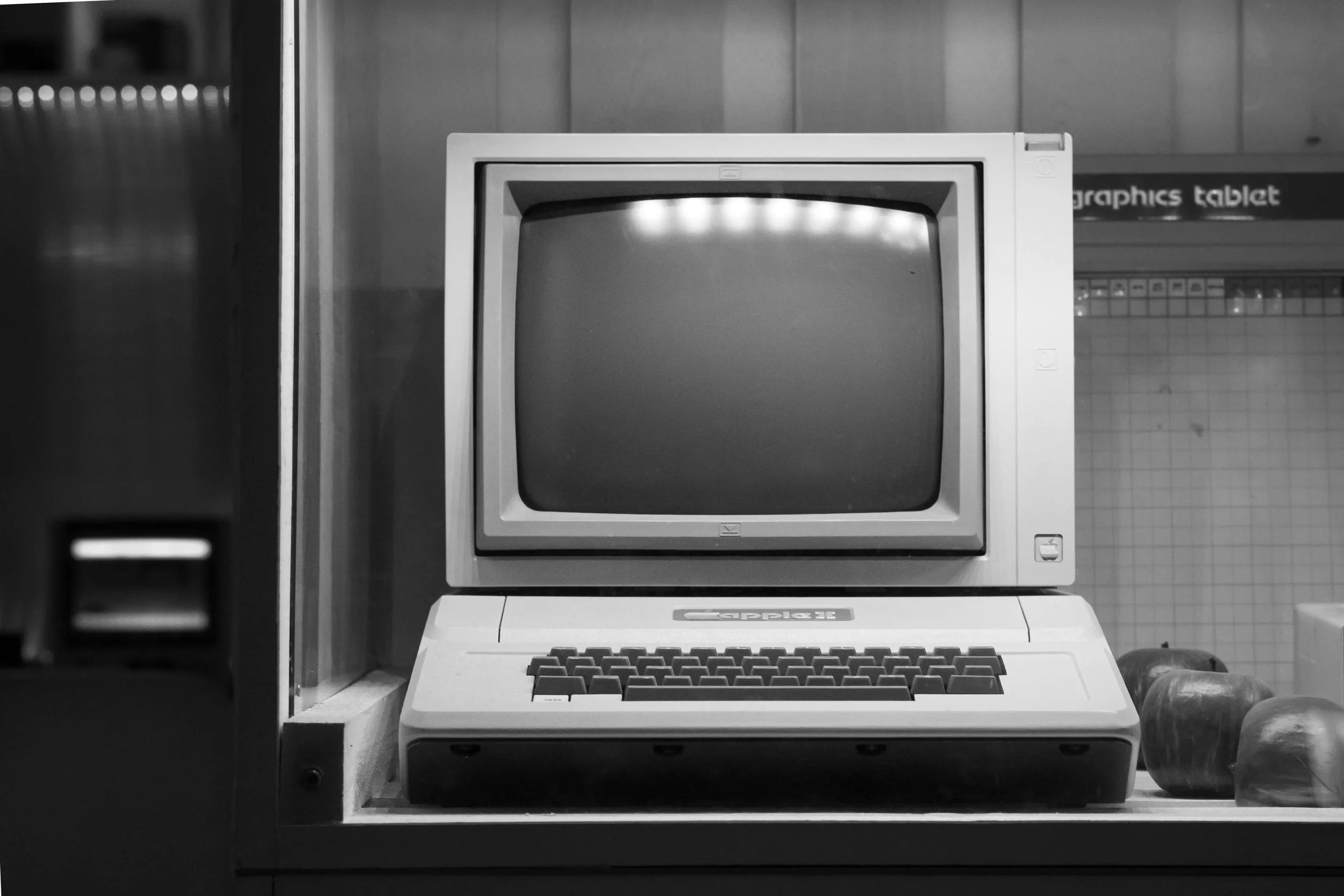 Black and white photo of an old computer monitor and keyboard on a display shelf.