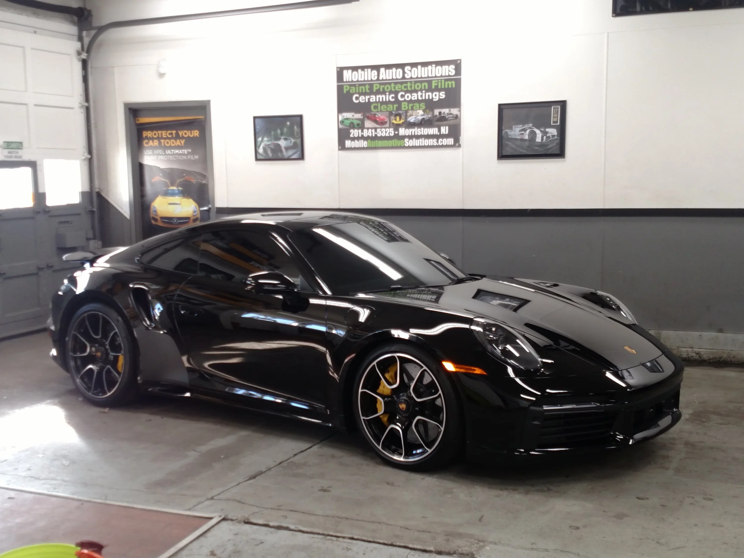 Black Porsche sports car parked in an indoor garage with signs about auto solutions on the wall.