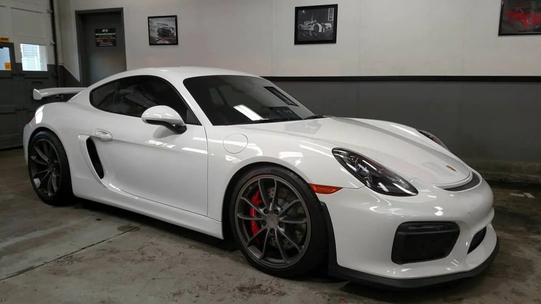White Porsche sports car parked indoors with black rims and red brake calipers.
