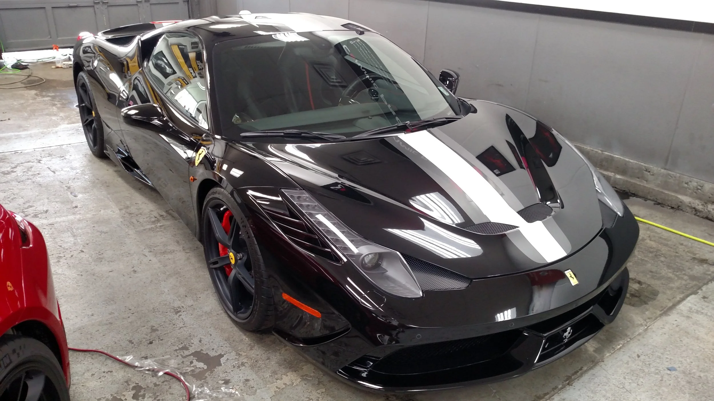 A black Ferrari sports car with a white racing stripe parked inside a garage.