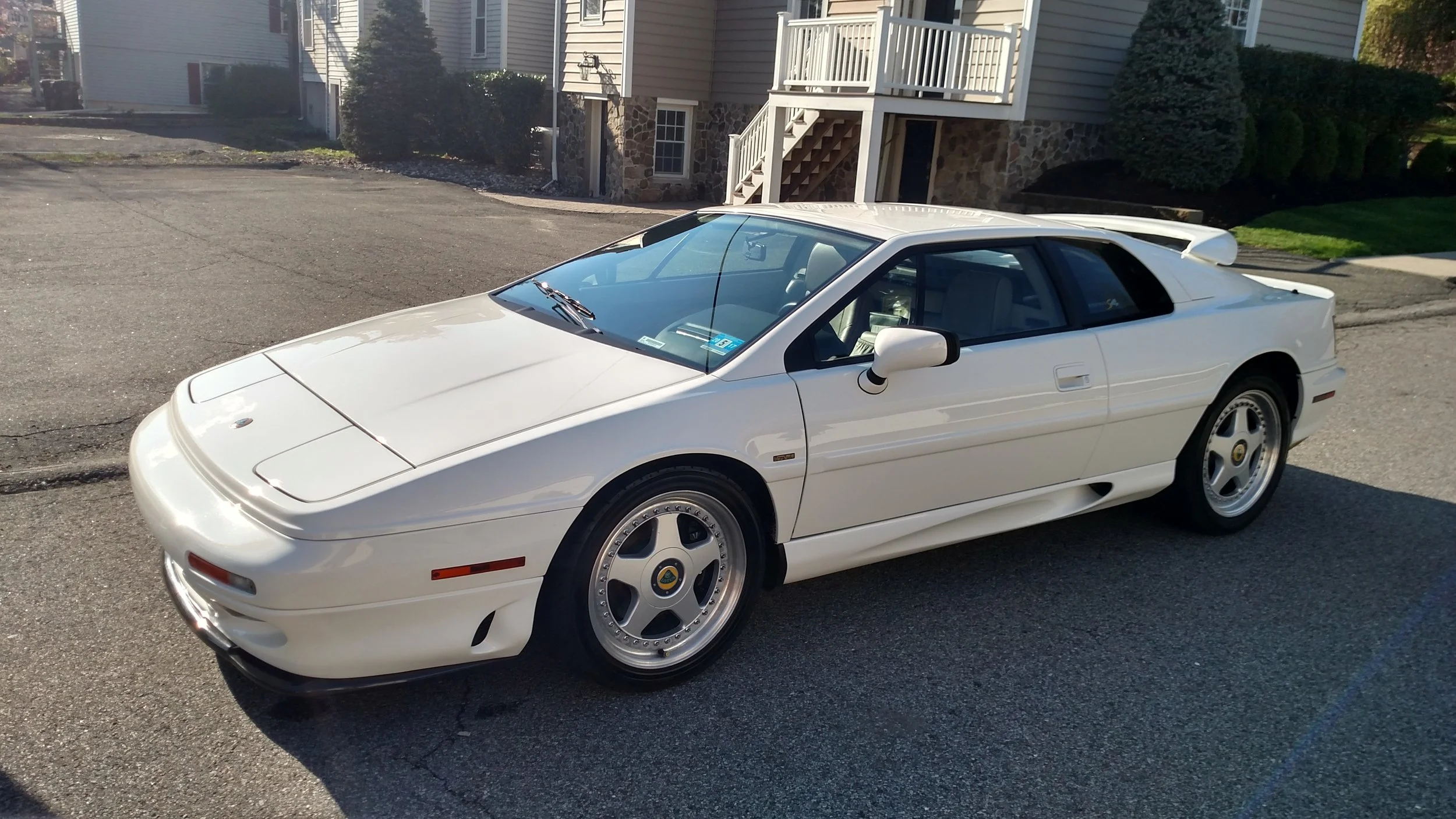 A white vintage Lotus Esprit sports car parked on a residential street in front of houses with manicured lawns.