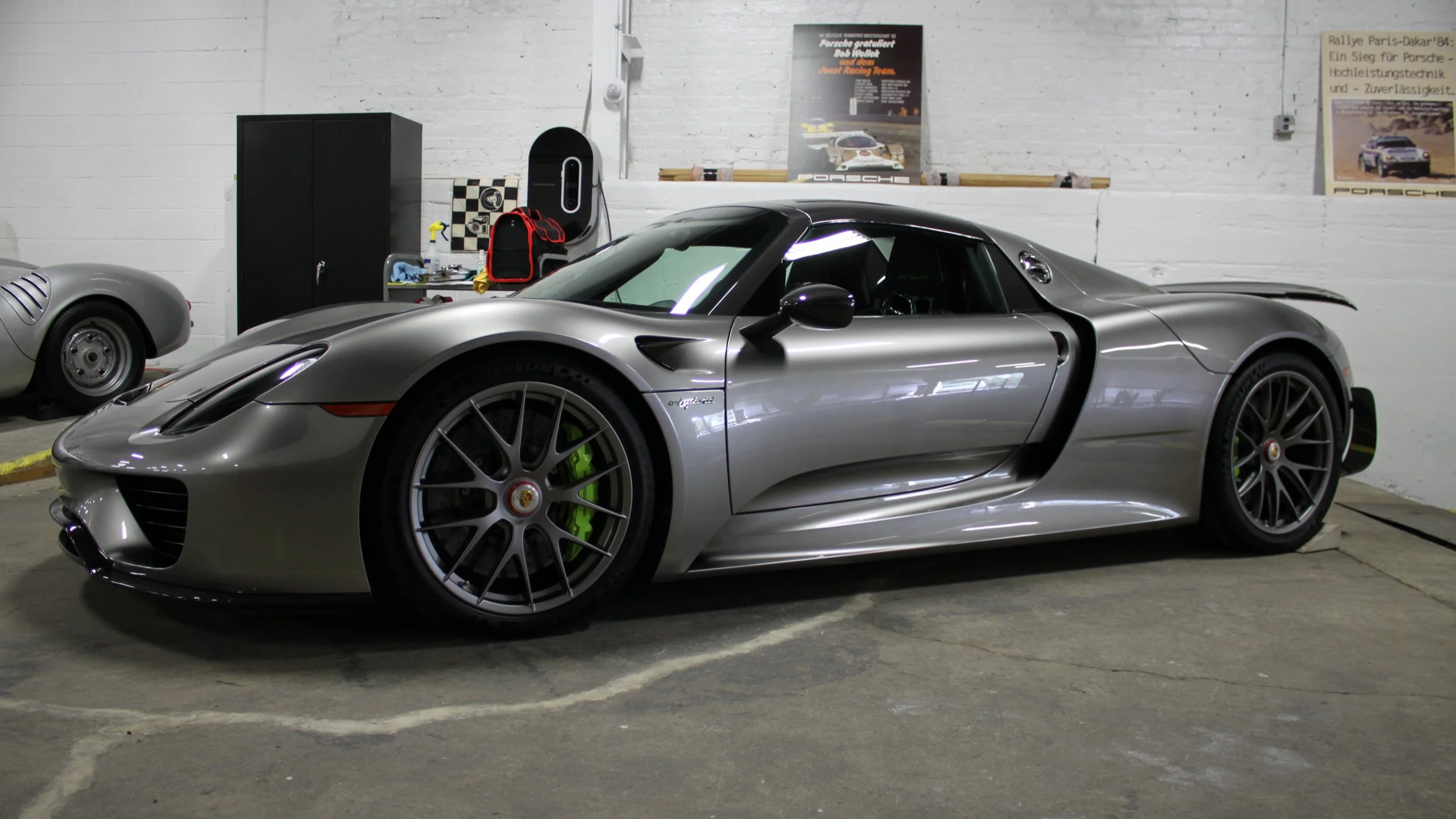 A silver Porsche 718 sports car inside a garage with white brick walls.