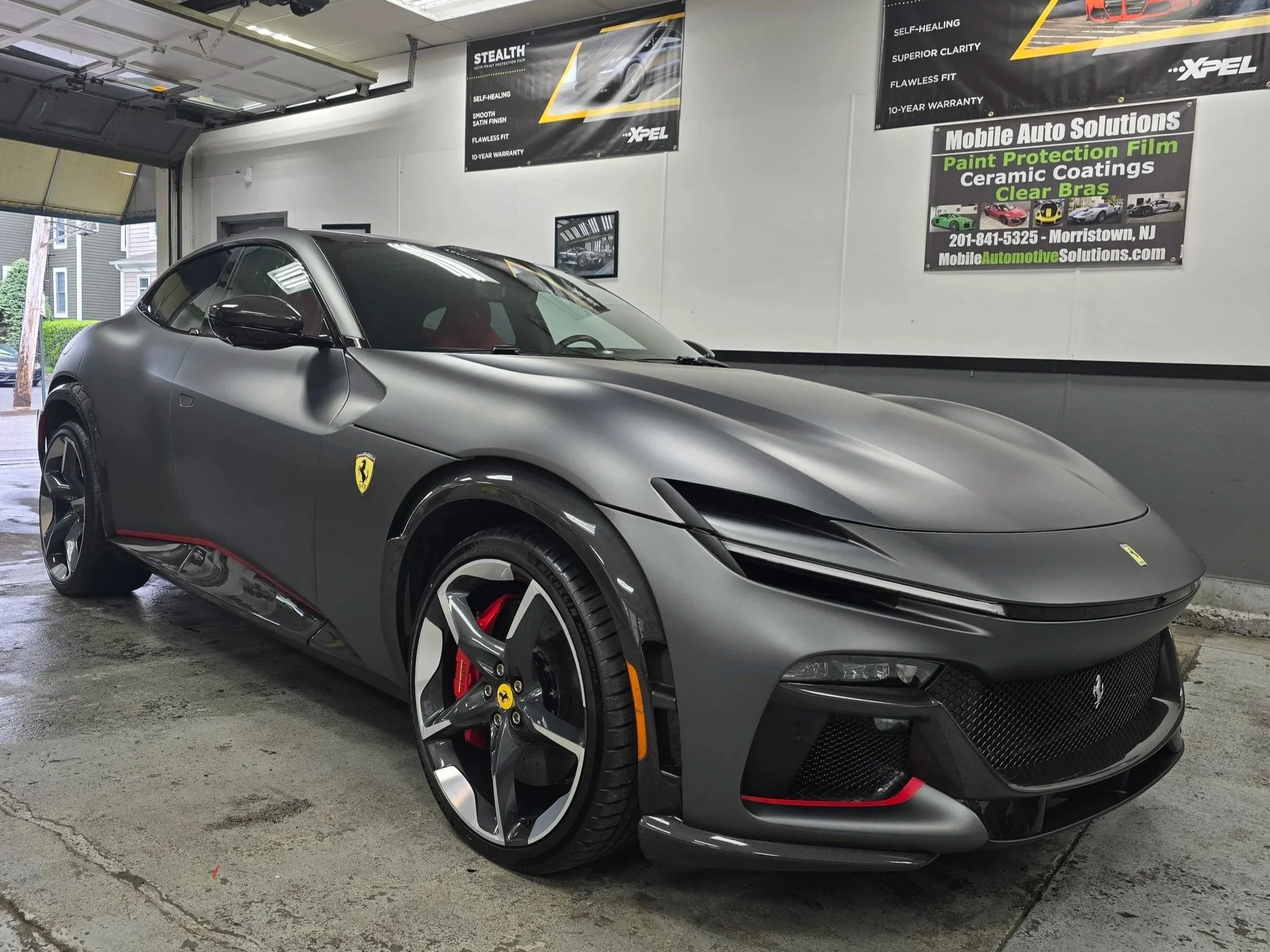 A sleek, matte gray Ferrari sports car with black and red accents.  Fully Wrapped in XPEL Stealth Film