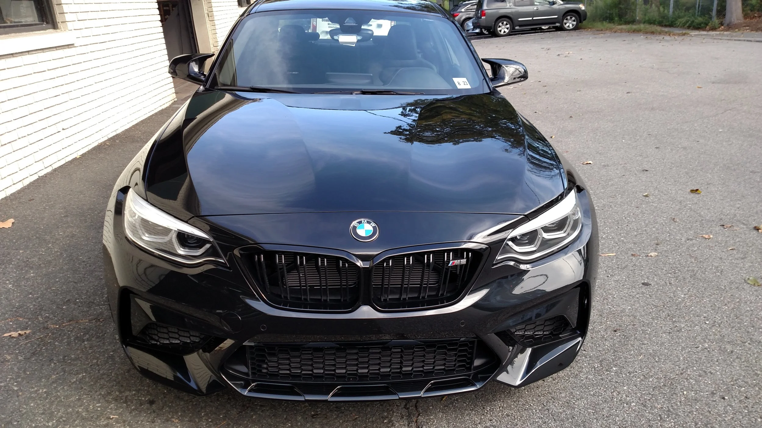 Front view of a black BMW car parked outdoors next to a white brick wall.