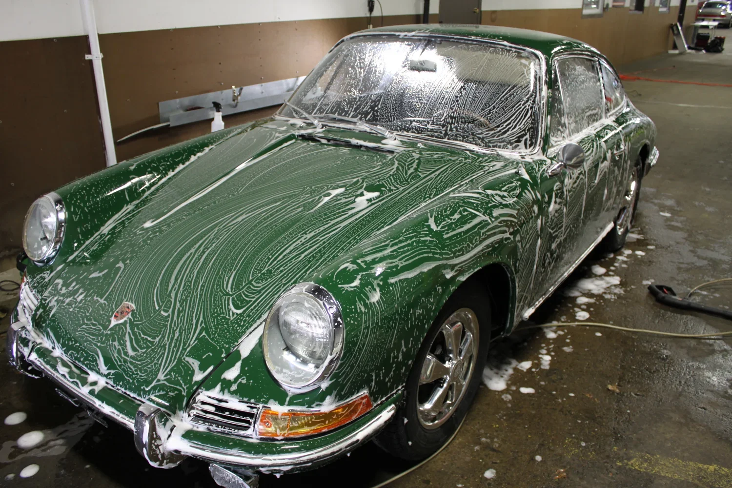 A green vintage sports car covered in soap suds during a car wash.