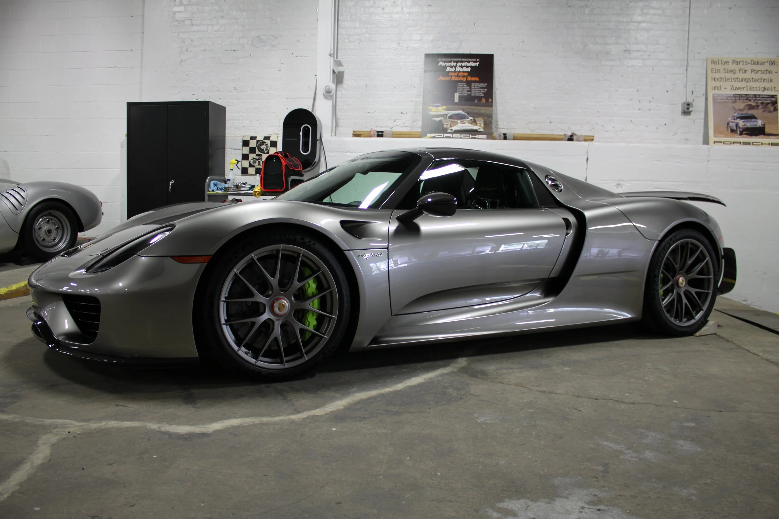 A silver Porsche 718 Cayman GT4 parked inside a garage with racing graphics on the wall.