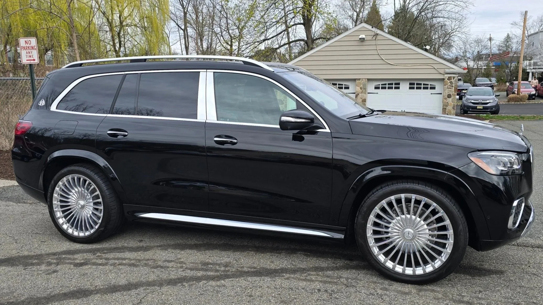 Black luxury SUV parked on the street with a residential house and other vehicles in the background