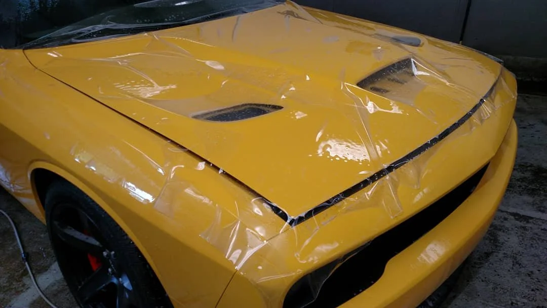 Yellow sports car with a damaged hood covered with protective plastic.