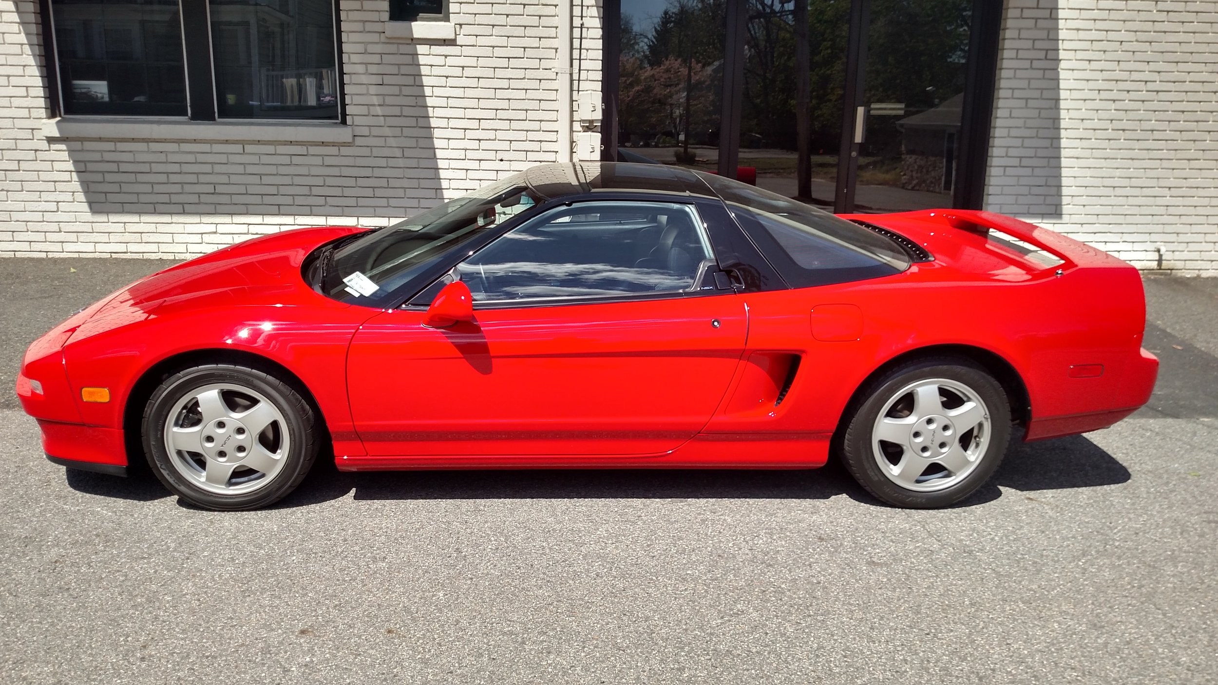 Red sports car parked on the street in front of a white brick building.