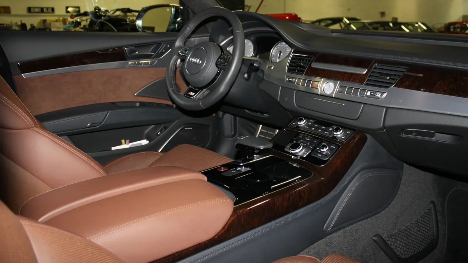 Interior of a luxury car, featuring brown leather seats, a dashboard with wood trim, and a steering wheel with Audi logo
