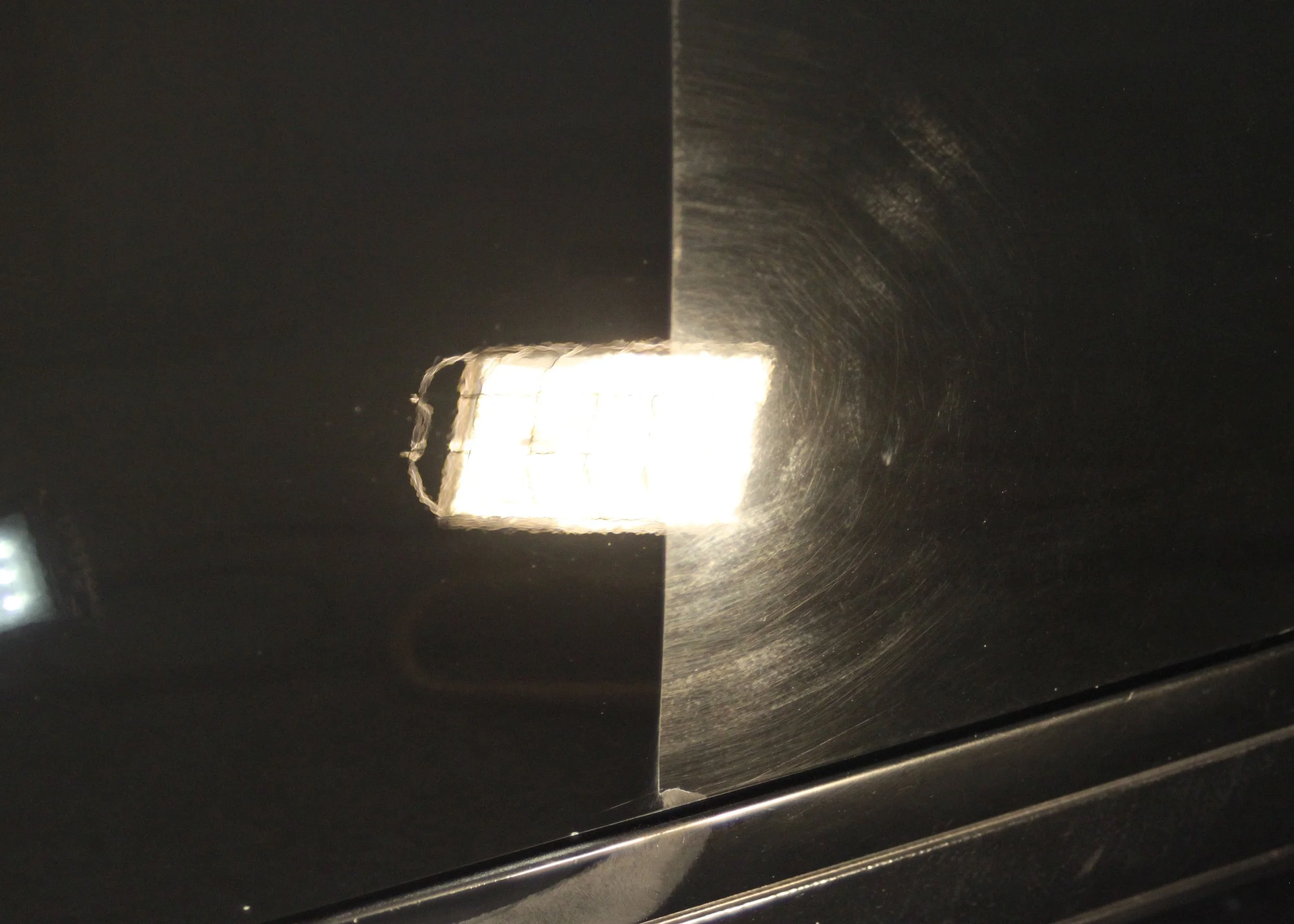 Close-up of a metallic surface with a rectangular bright spot, showing scratches and a dent near the center.