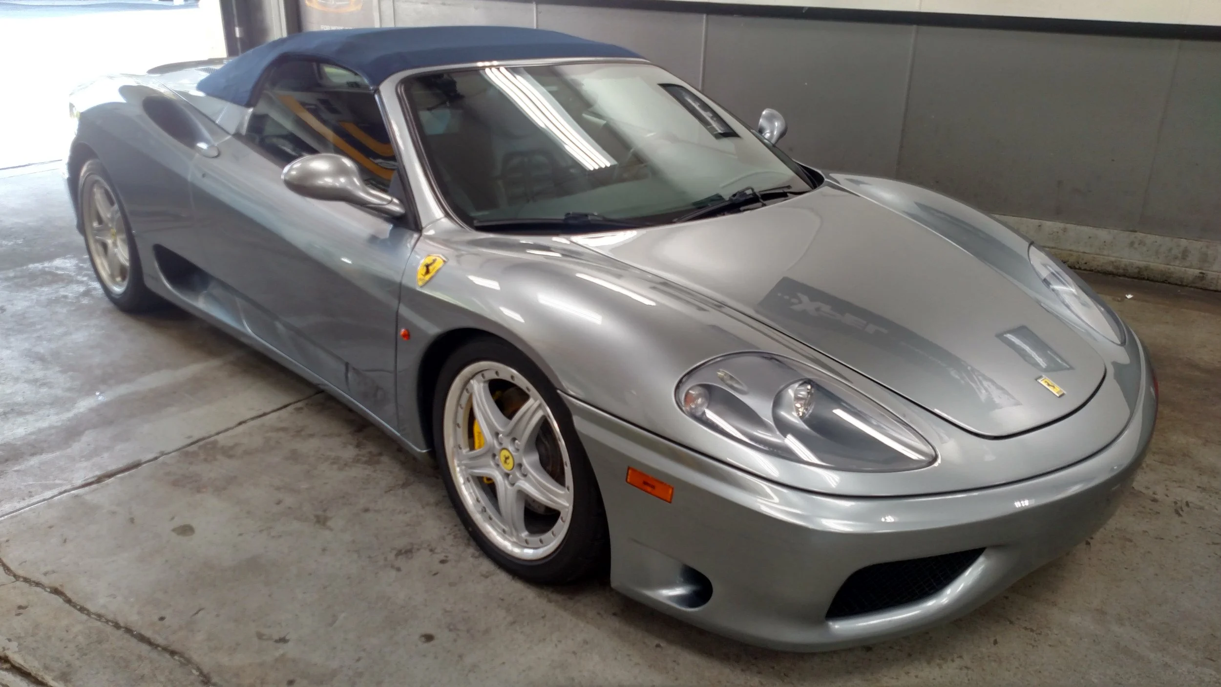 A silver Ferrari sports car with a blue convertible top parked inside a garage.