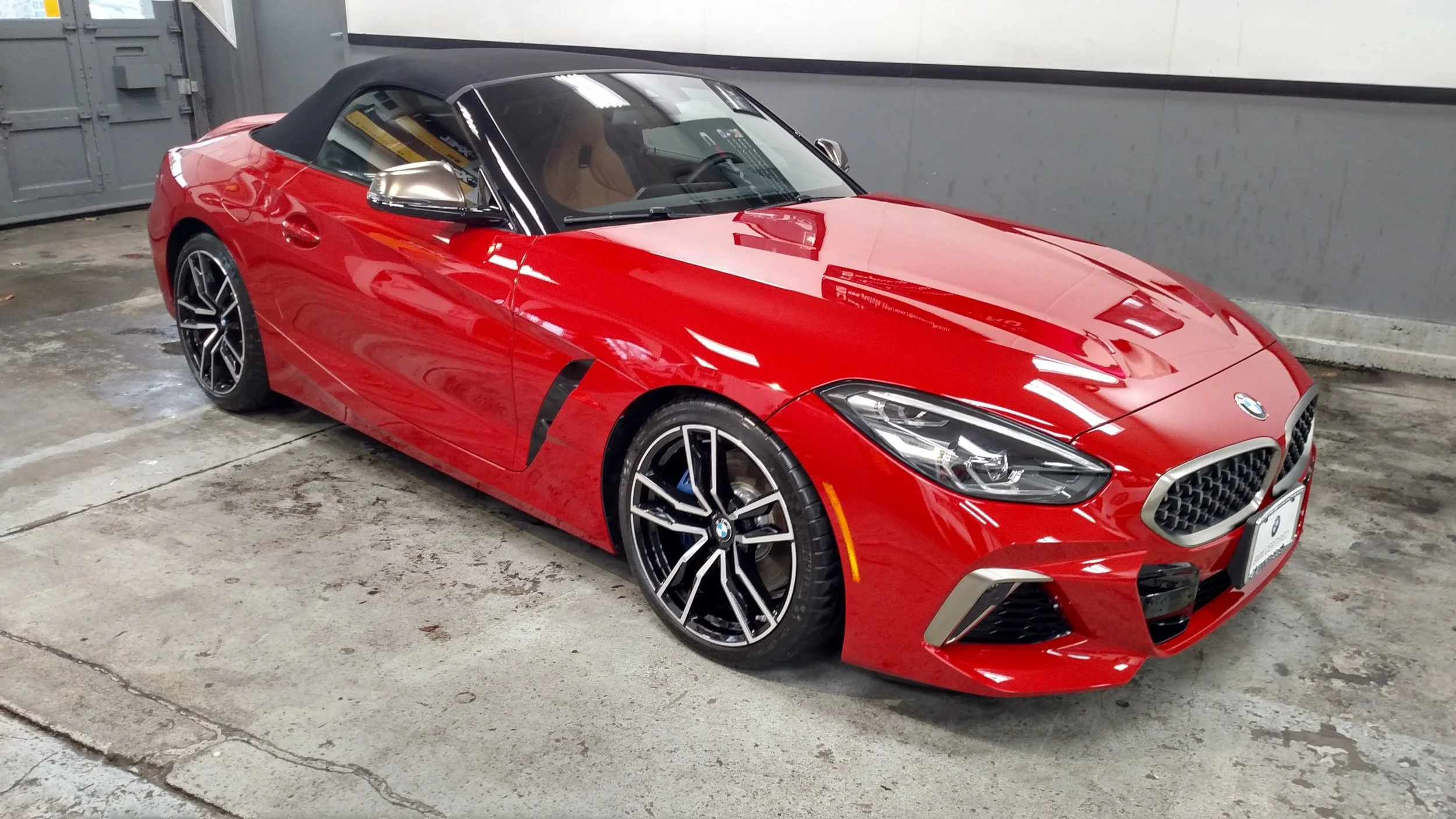 Red BMW convertible with black soft top, parked in an indoor parking space.