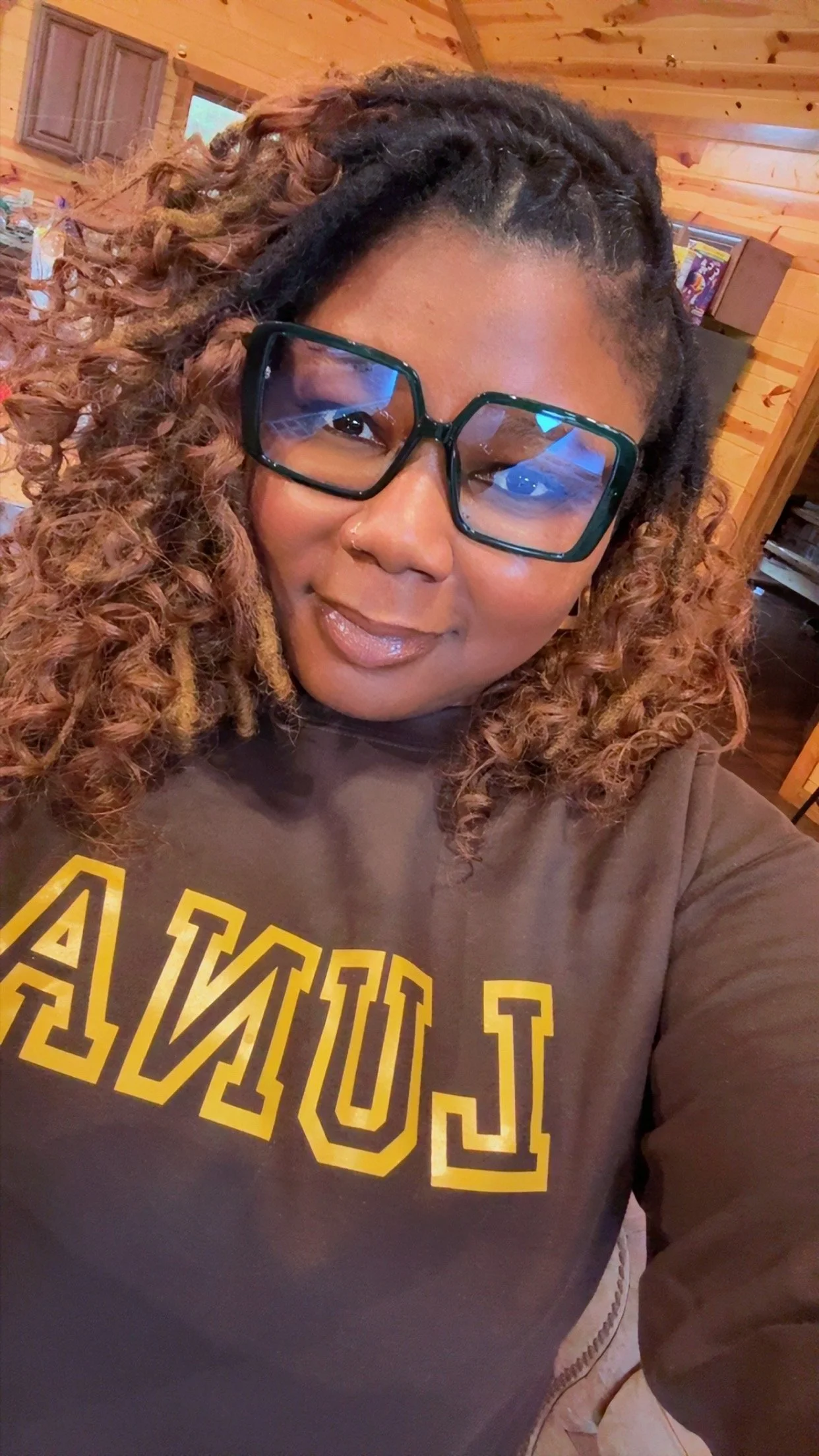 A woman standing in front of a balloon arch, reaching out with her left hand. She is dressed in a yellow jacket, white shirt, black pants, and a yellow beret.