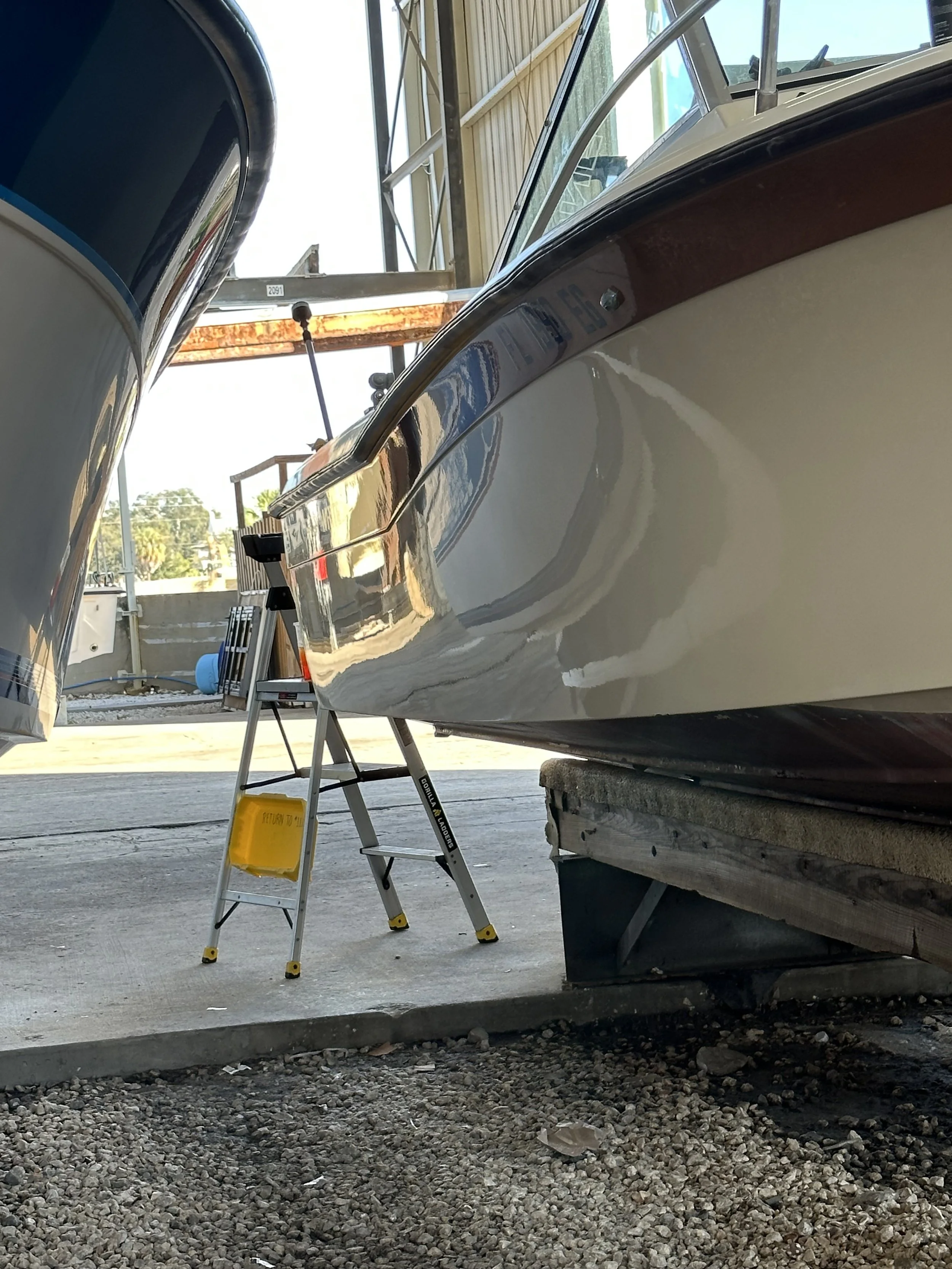 A boat is on a lift in a boatyard, with a ladder and a yellow caution sign nearby.