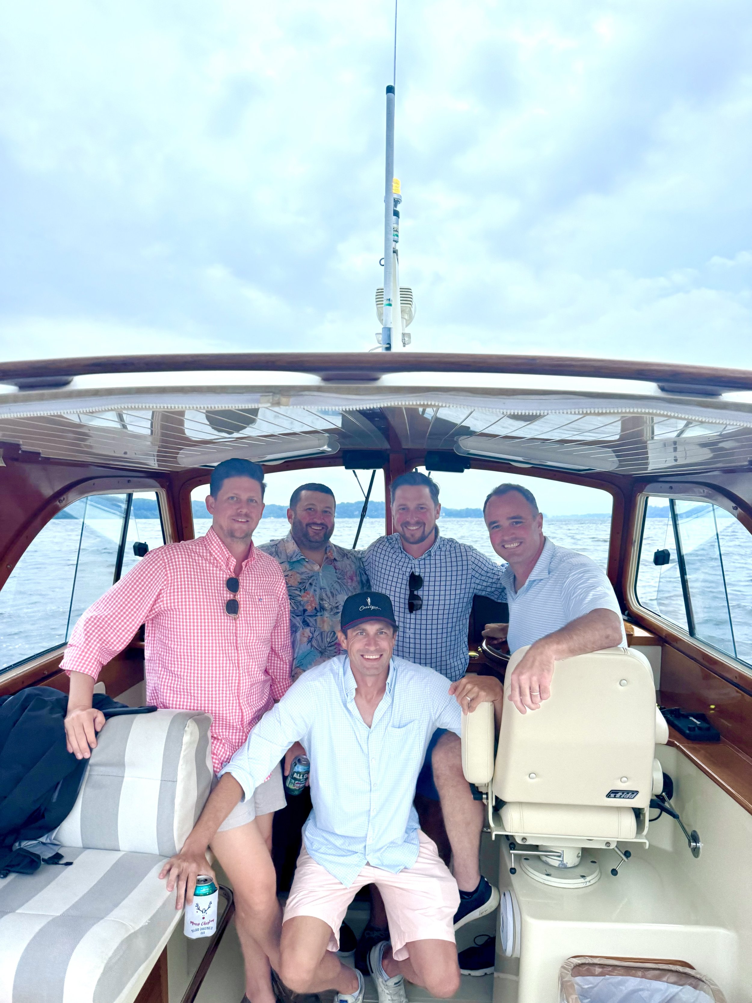 Group of men on a boat, smiling and posing, with one seated and holding drinks.