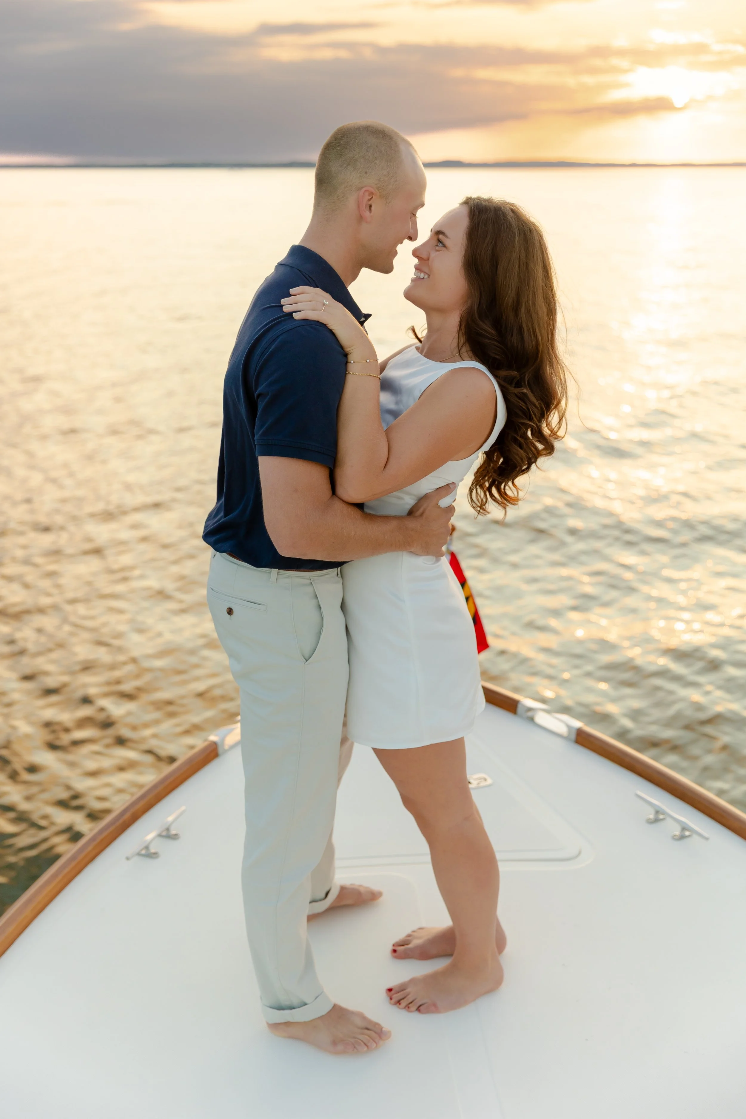 A couple celebrating their engagement on the bow of our Hinckley Picnic Boat during a private luxury sunset charter with Chesapeake Classic Yacht Charters with the sunset and Chesapeake Bay are in the background. Photo courtesy of Stephanie Wyvill Ph