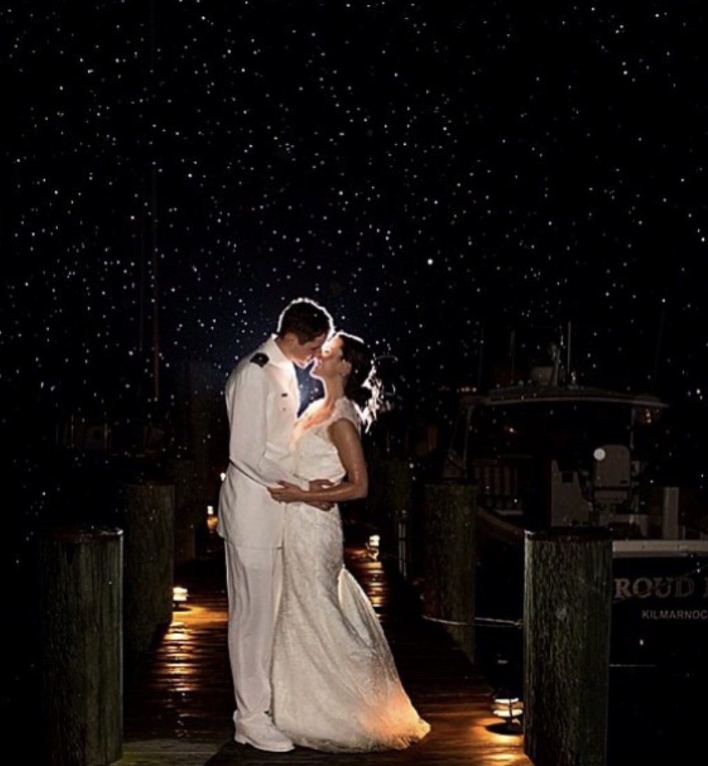 Bride and groom kissing under a starry sky on a dock.