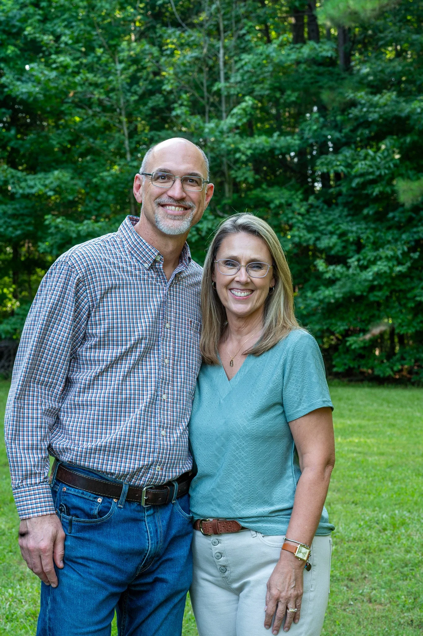 A middle-aged man and woman smiling outdoors in a lush green park.
