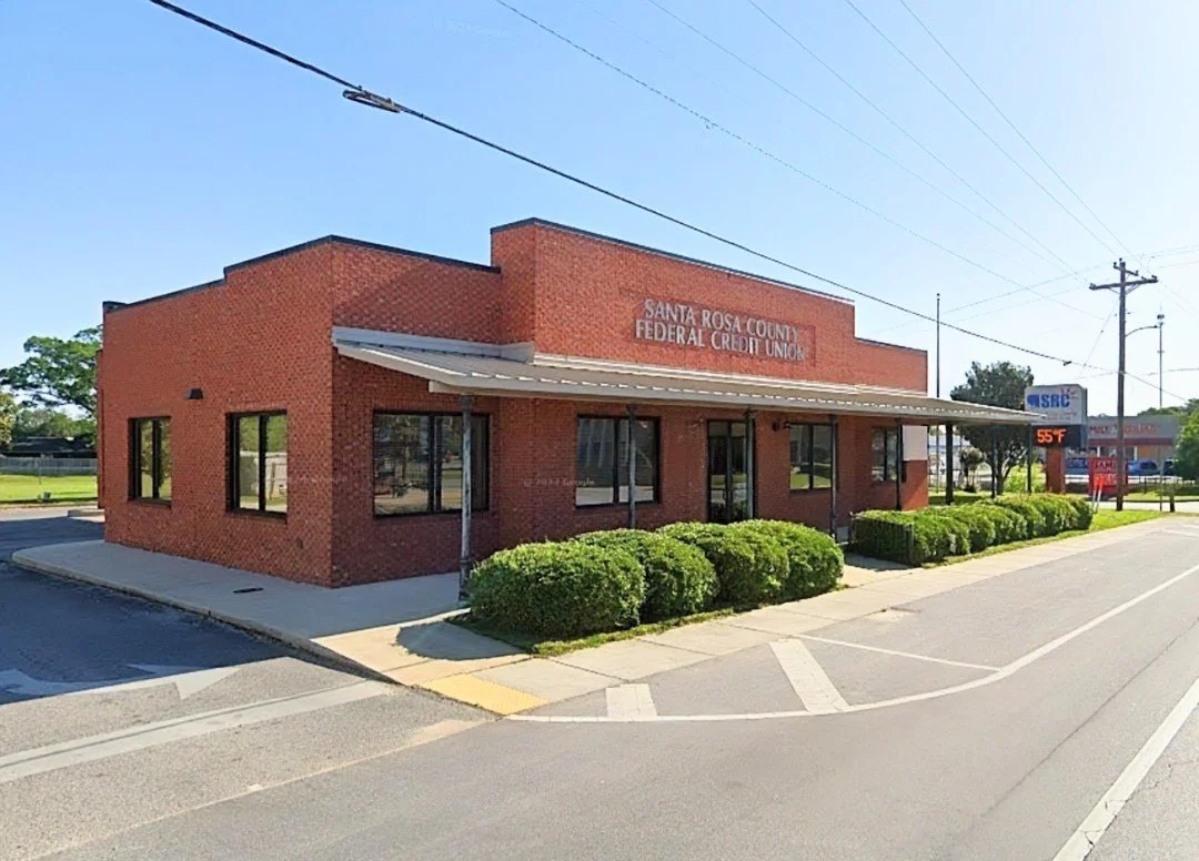 Santa Rosa County Federal Credit Union brick building exterior in Jay, Florida, with clear blue sky, sidewalk, and trimmed bushes along the front entrance.