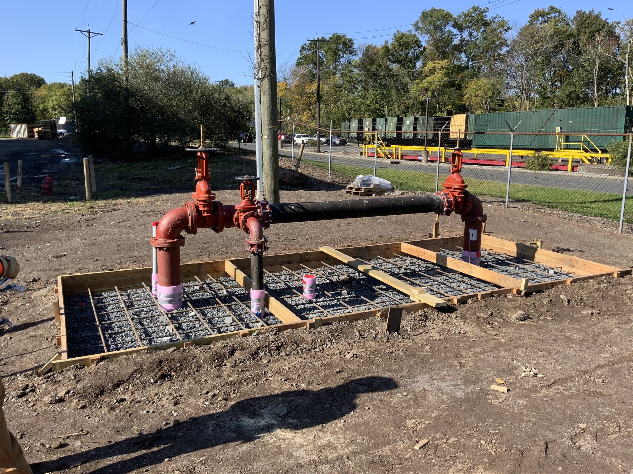 Underground pipe installation with red pipes, wooden frames, and metal rebar grid in a construction site.