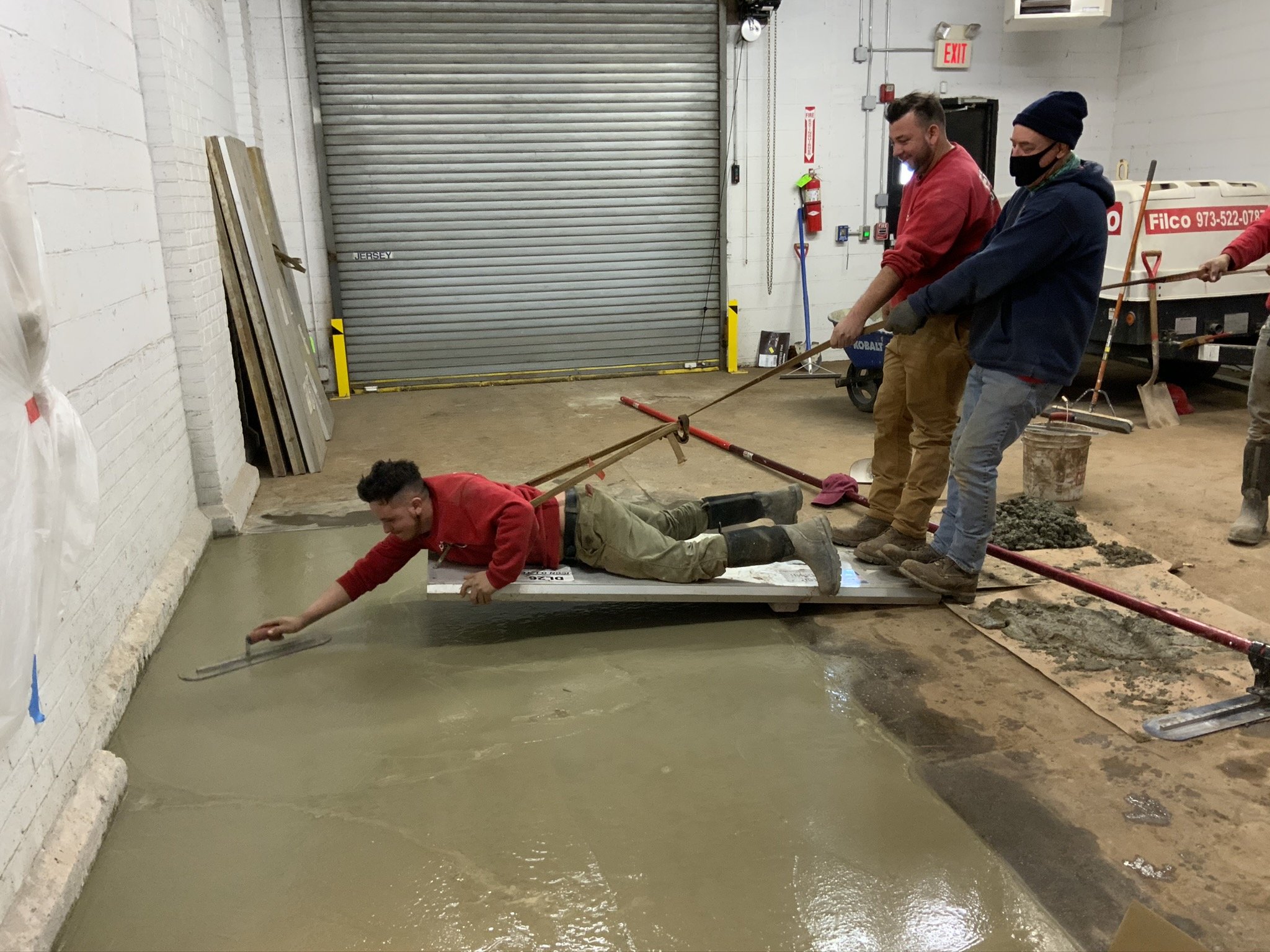 A group of workers pouring concrete on a construction site, with one person lying on a float to spread the concrete while others assist