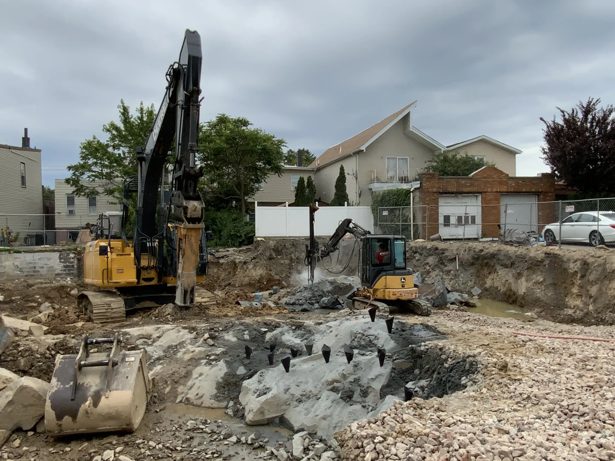 Construction site with excavators working on a foundation in a residential area, overcast sky.
