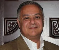 Woman in peach blazer smiling indoors with blurred background