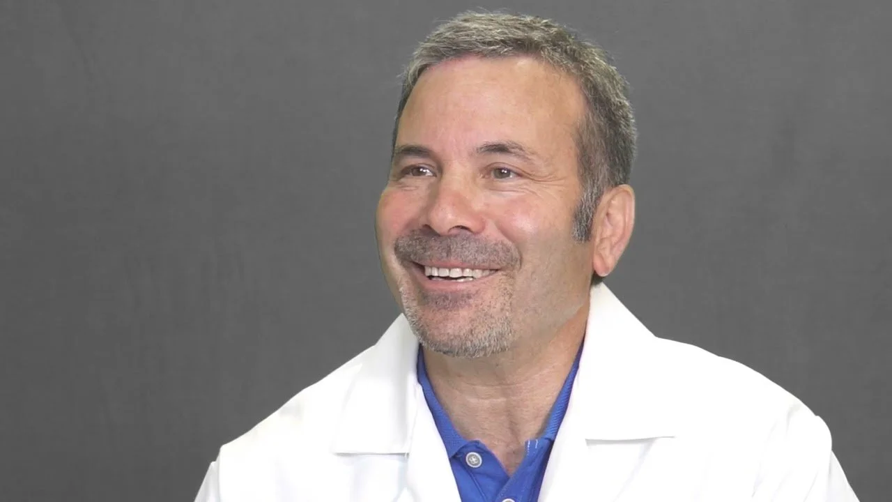 Male doctor with short gray hair, wearing glasses and a white coat with "Le Church, MD, MPH" embroidered on it.