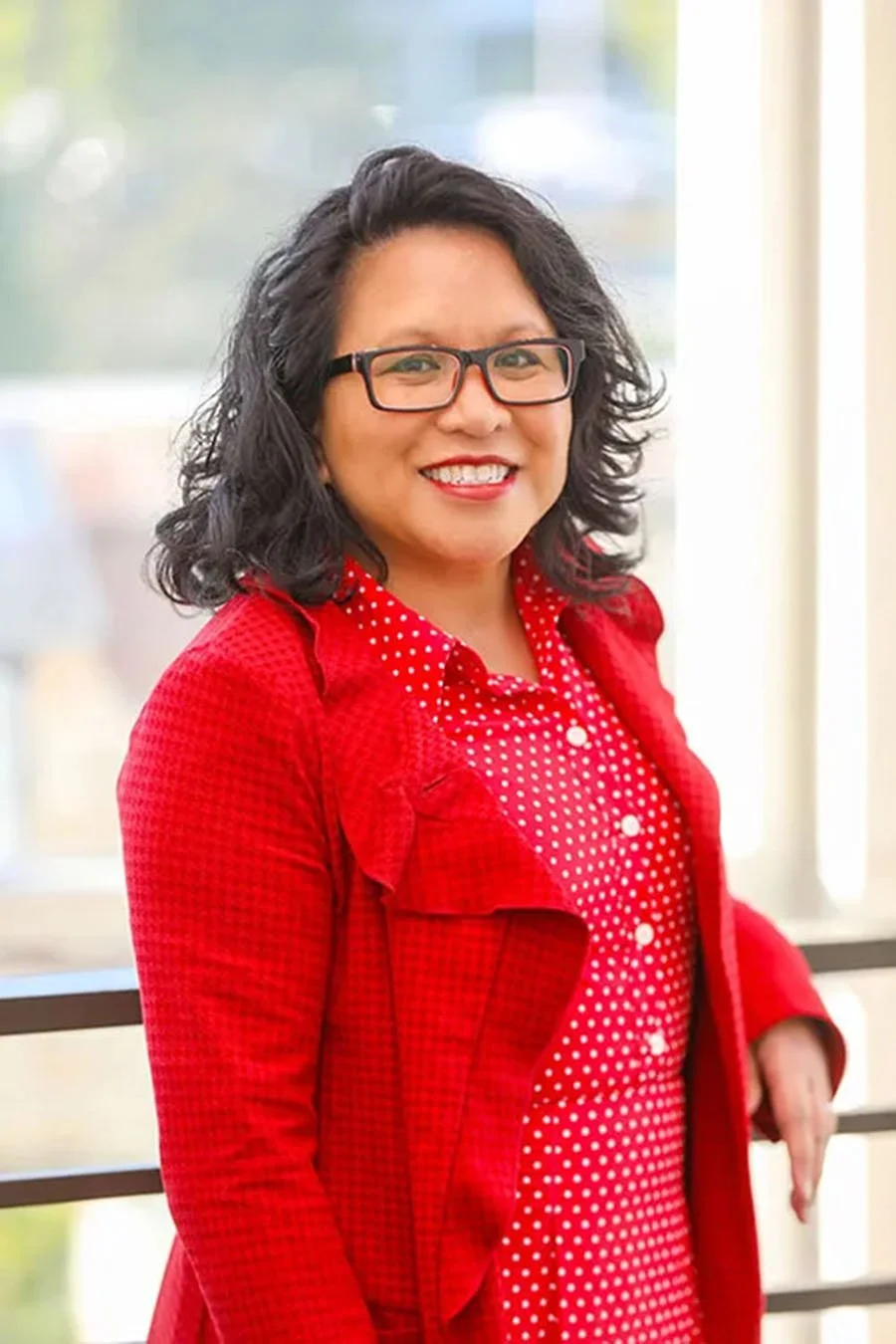 Person wearing glasses and a red polka dot outfit smiling indoors.