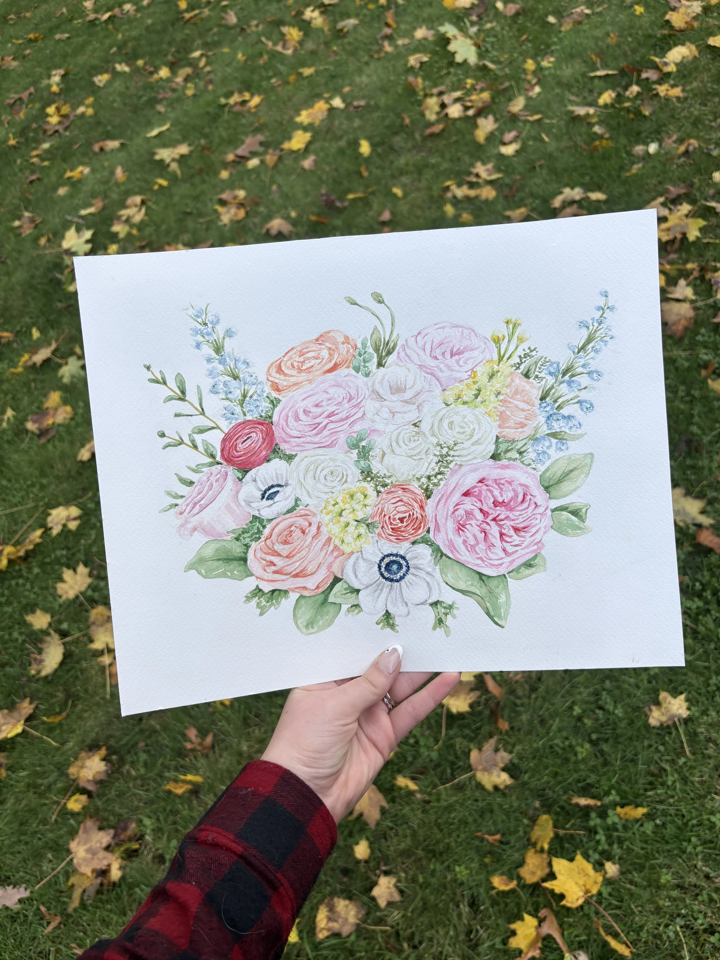 A watercolor painting of a bouquet of various flowers, including roses, anemones, and other blossoms, held in a person's hand against a background of fallen autumn leaves and green grass.
