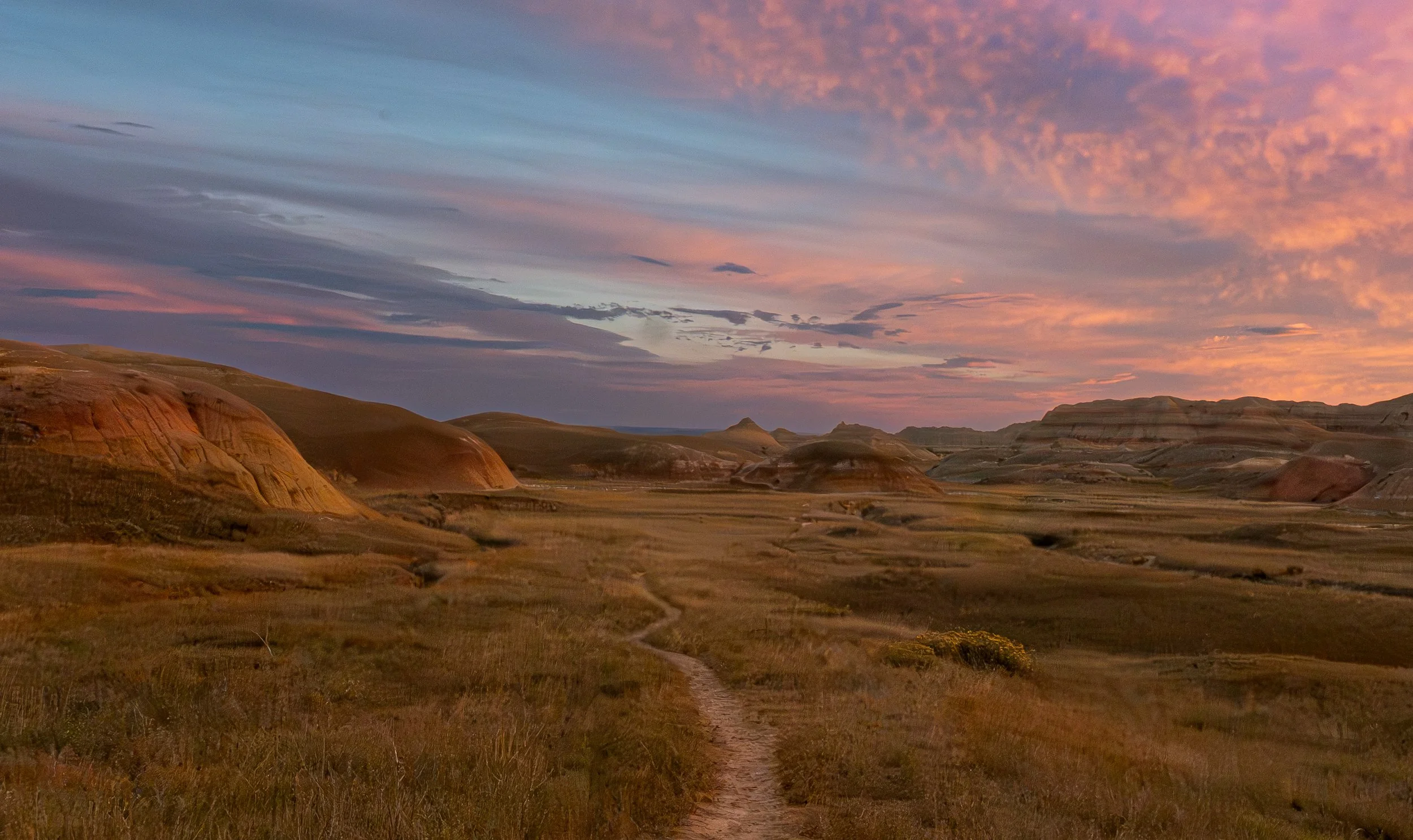 Picture of a winding trail through the Badlands National Park wilderness at sunset. Photographed by Jeff Pauley in late September 2026.