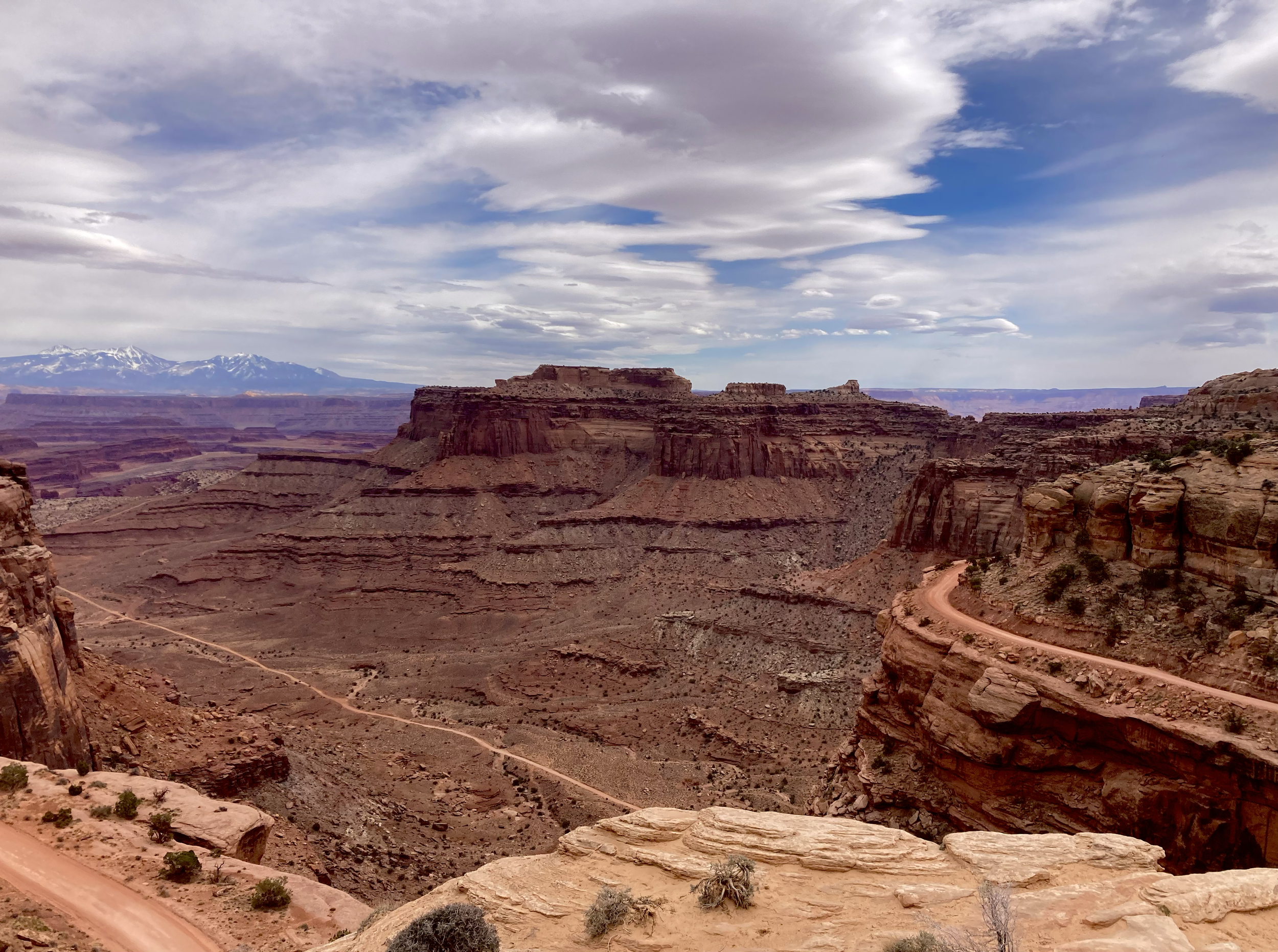 Photograph of a narrow dirt road winding along the edge of a deep canyon in Souther Utah. Hues of brown and blue.