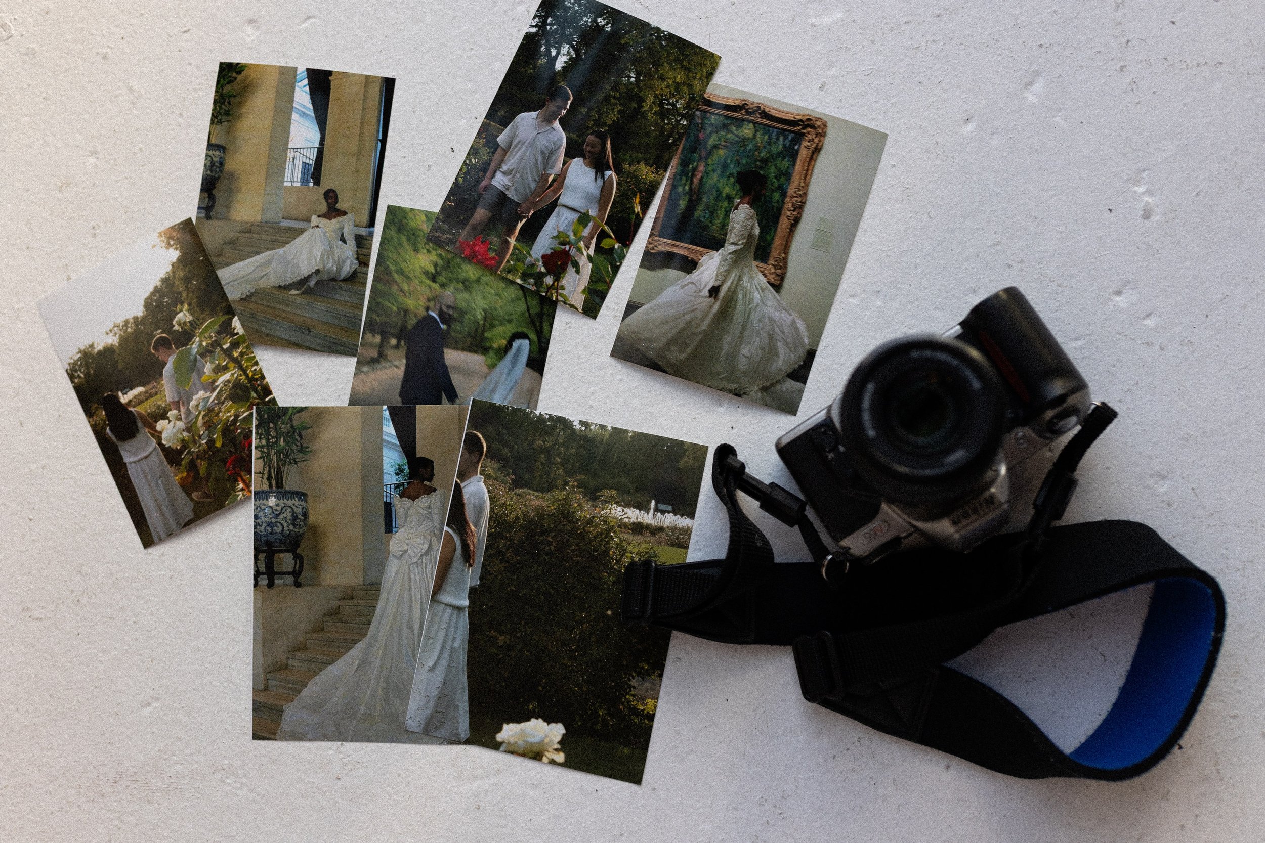 A collection of wedding and romantic photographs laid out on a surface beside a vintage camera. The photos feature couples during a wedding or engagement, with settings including gardens and art galleries.