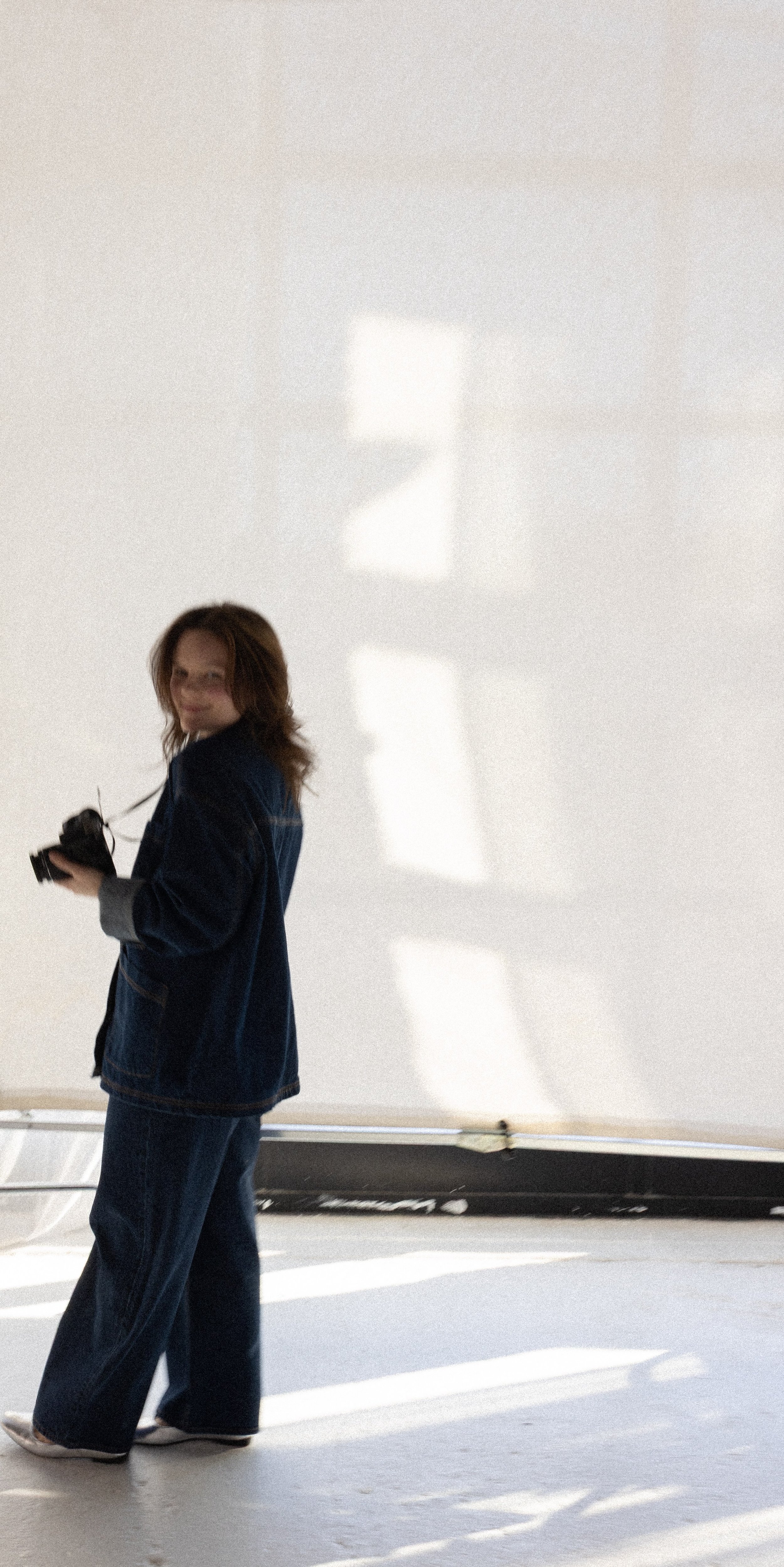 Person in denim holding a camera in a sunlit room.