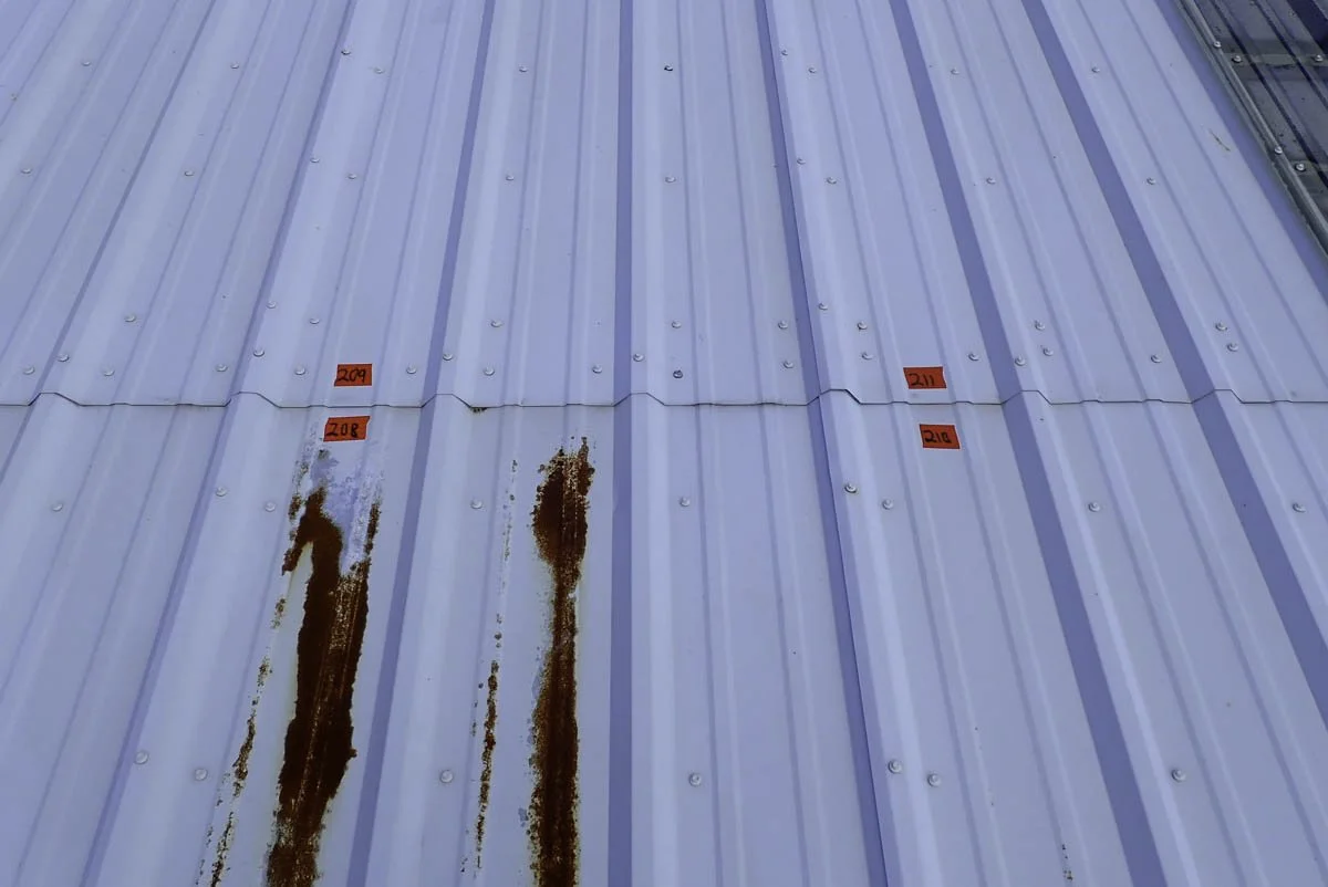Blue metal roof with rust stains and red tags labeled 209, 208, 211, and 210 in red